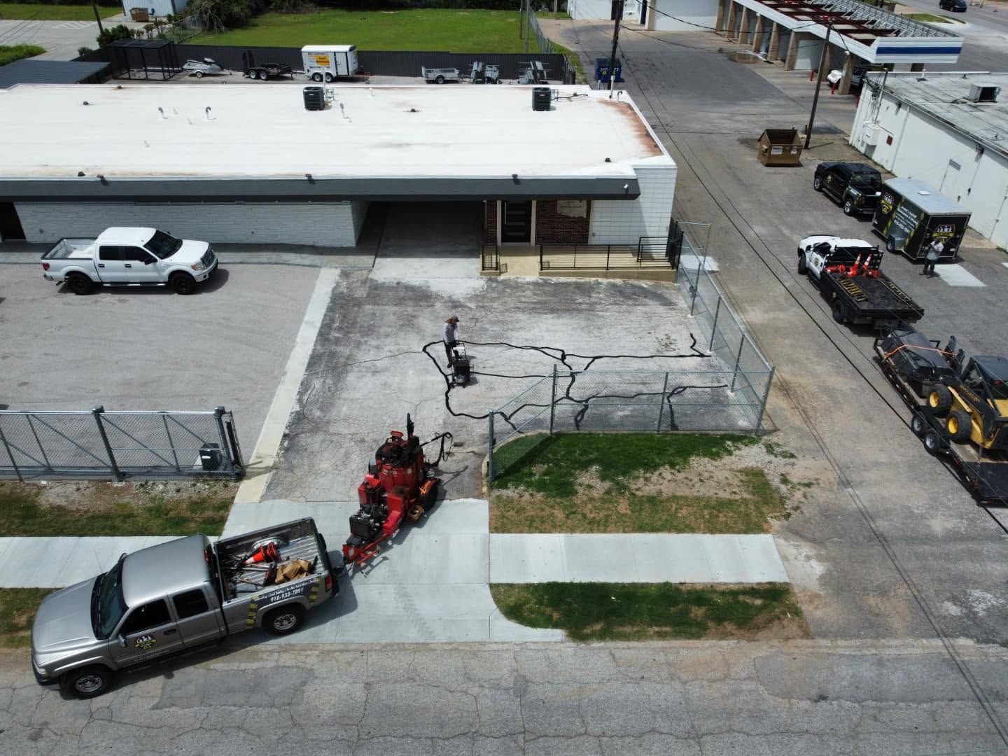 Overhead view of a tow truck lifting a silver pickup in a paved industrial lot beside a warehouse