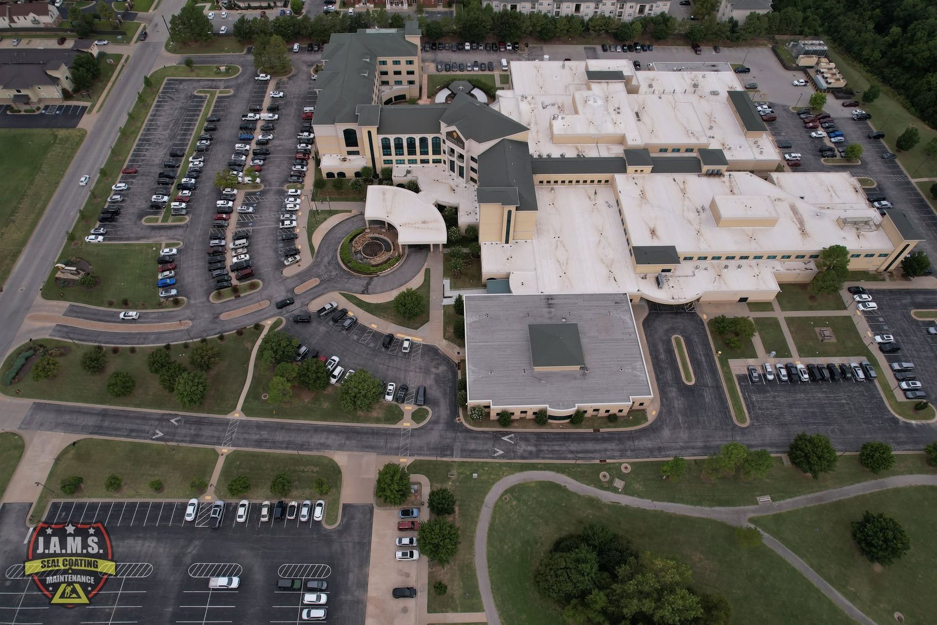 Aerial view of a large office or school complex with parking lots, roads, and surrounding trees.