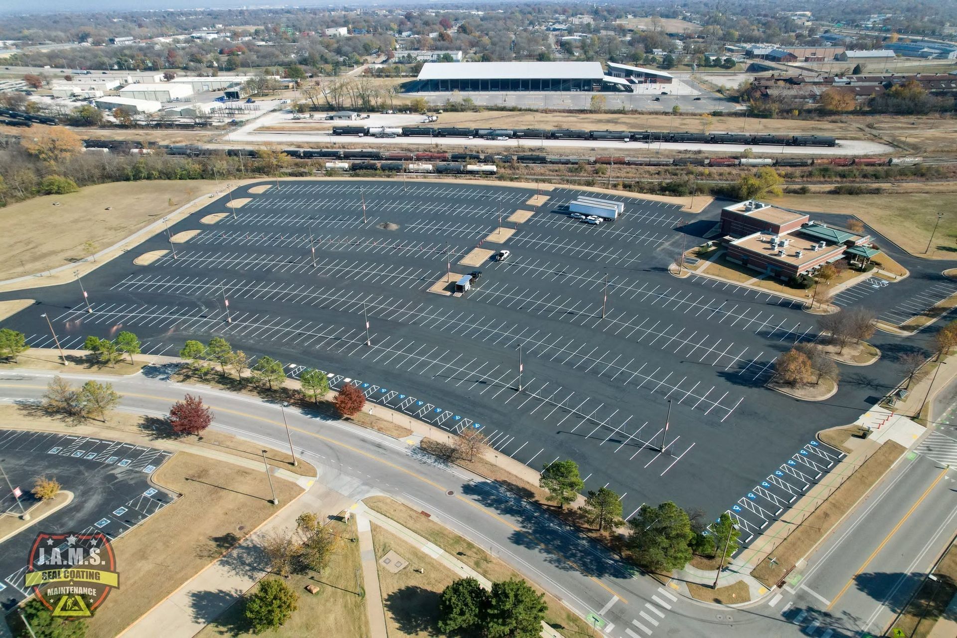 Aerial view of a mostly empty parking lot beside commercial buildings and roads in a suburban area