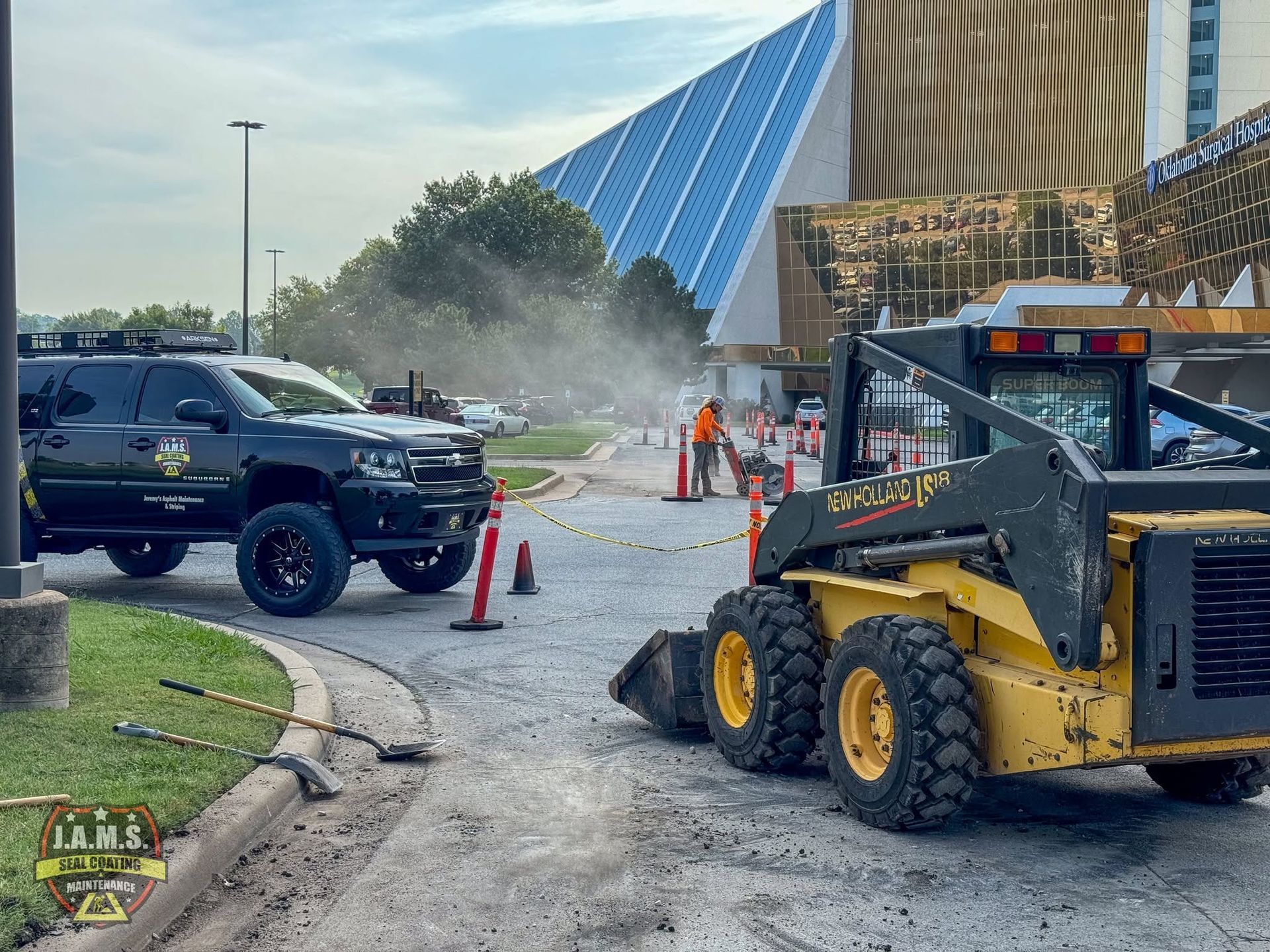 Construction cleanup with skid steer, pickup truck, cones, and spray mist outside a building