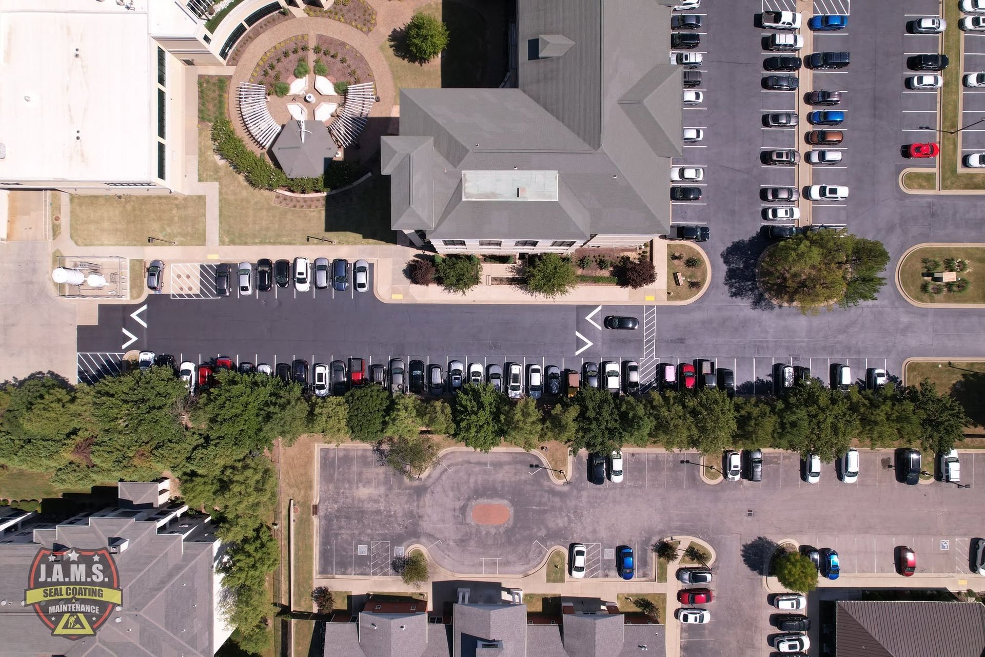 Aerial view of a parking lot, buildings, and trees along a street.