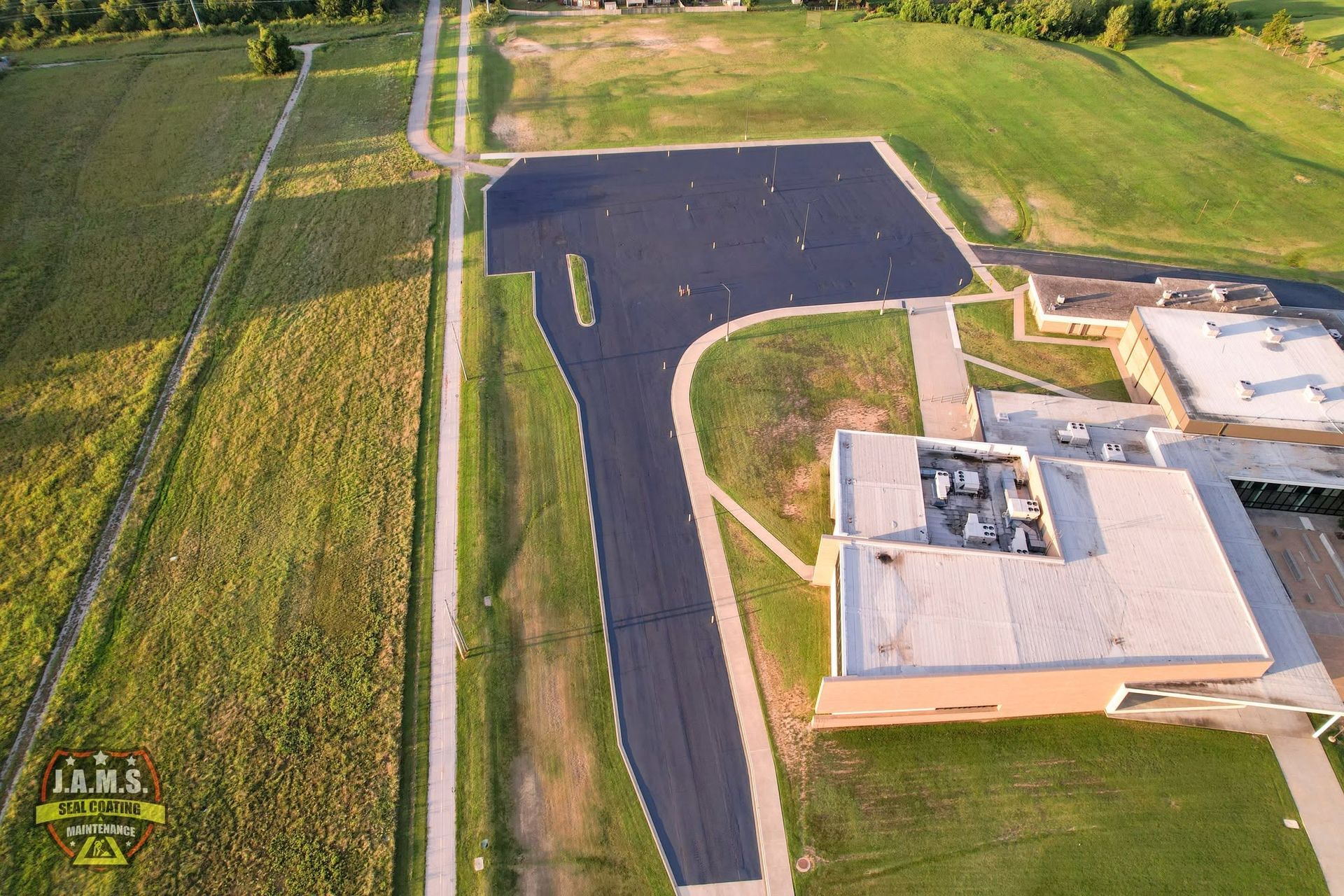 Aerial view of a new black asphalt driveway beside a building and grassy fields.