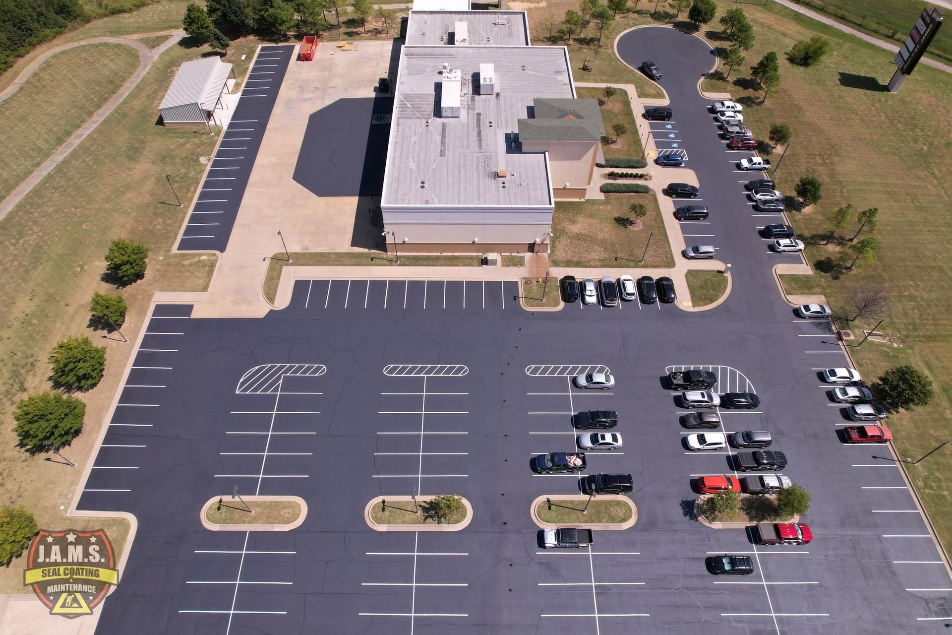 Aerial view of a building with a mostly empty parking lot and parked cars on the right side