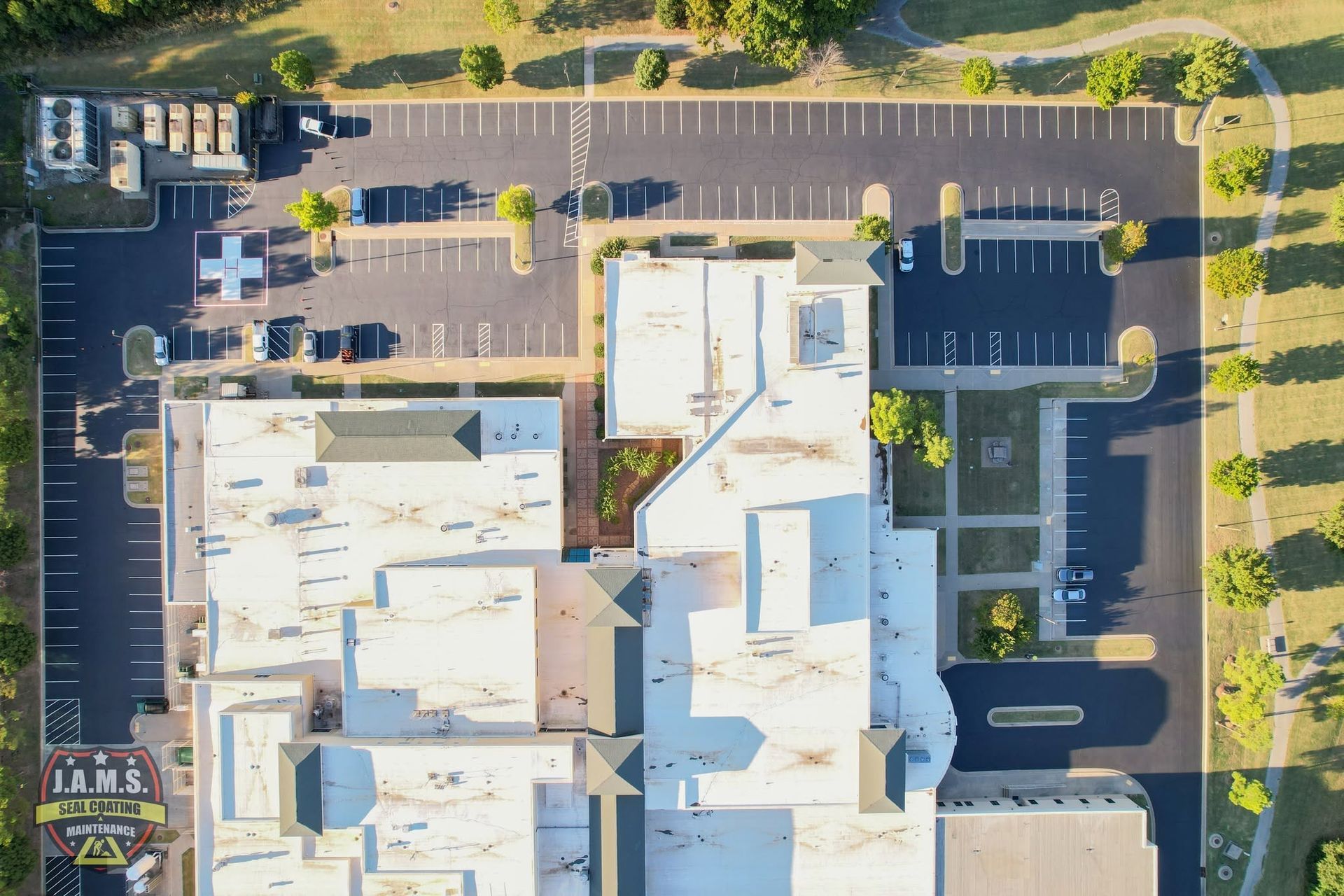 Aerial view of a white-roofed commercial building with surrounding parking lots and trees