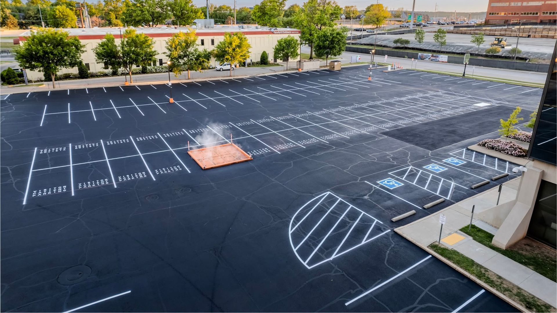 Empty black parking lot with white parking lines and a small orange tarp, bordered by trees and buildings