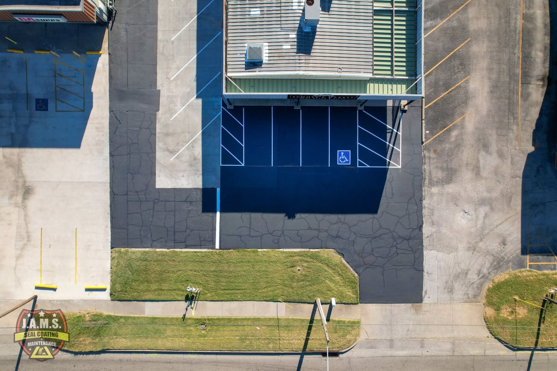 Aerial view of a blue-roofed building with a small parking lot, sidewalk, and grassy strip.