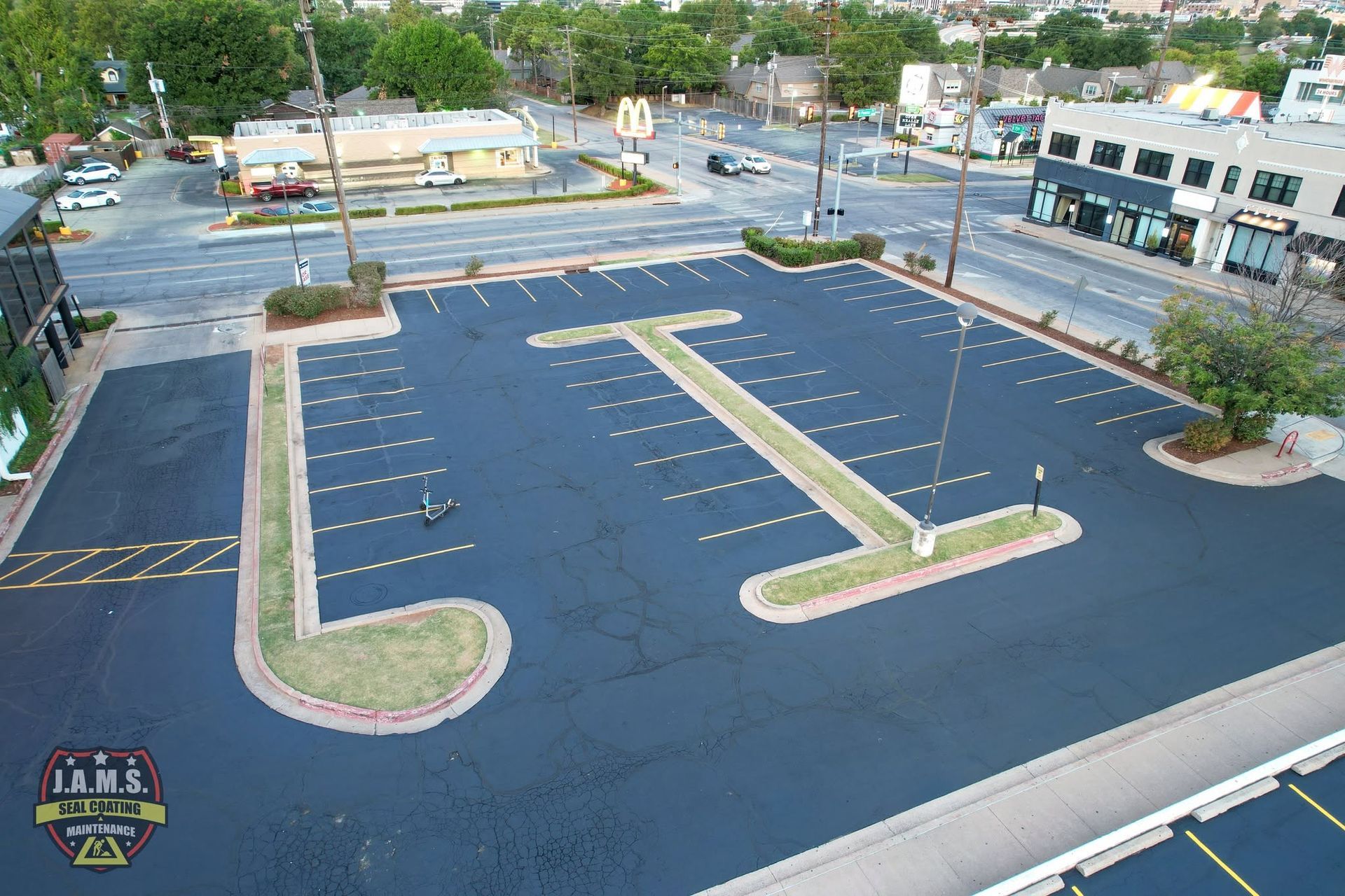Empty blue parking lot with painted lane markings and a landscaped island in front of storefronts
