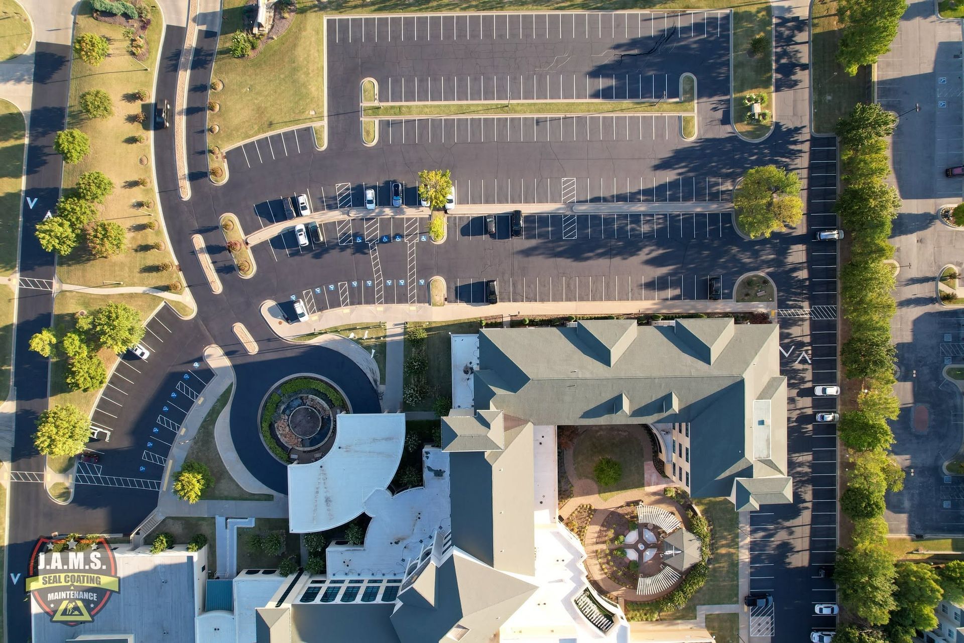 Aerial view of a building with parking lot, cars, trees, and sidewalks in bright daylight