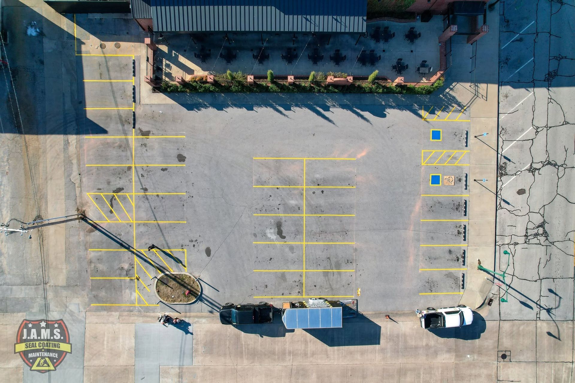 Overhead view of a mostly empty parking lot with yellow-marked spaces, a few parked cars, and a building edge.