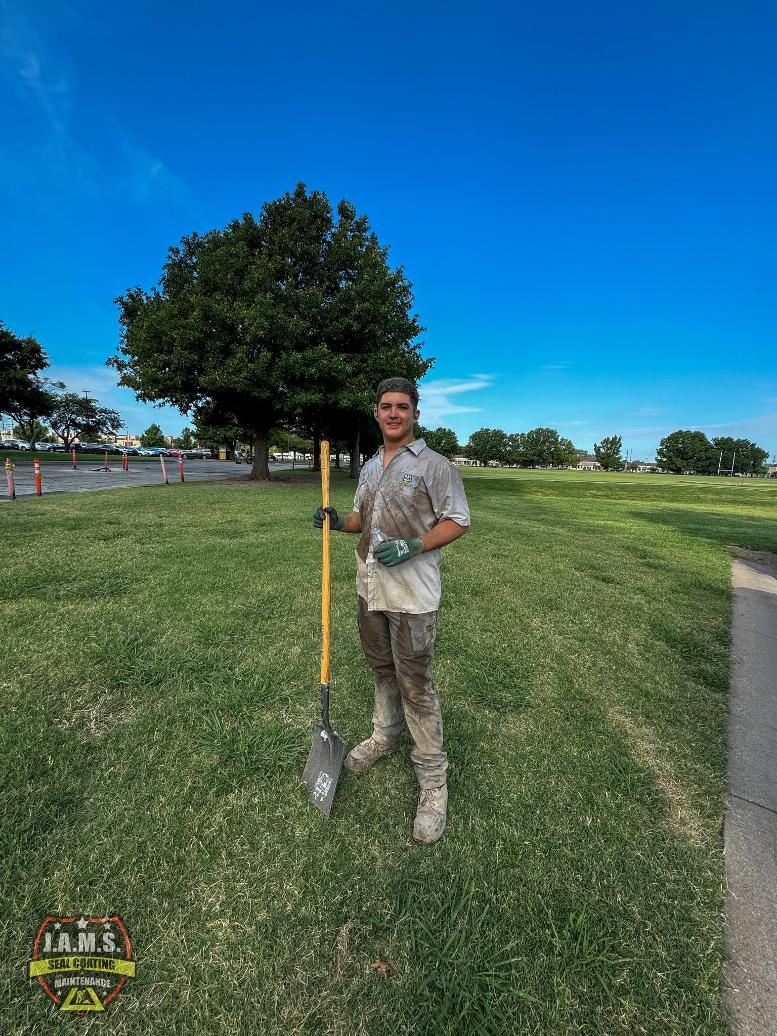 Person holding a shovel on a grassy field under a bright blue sky.