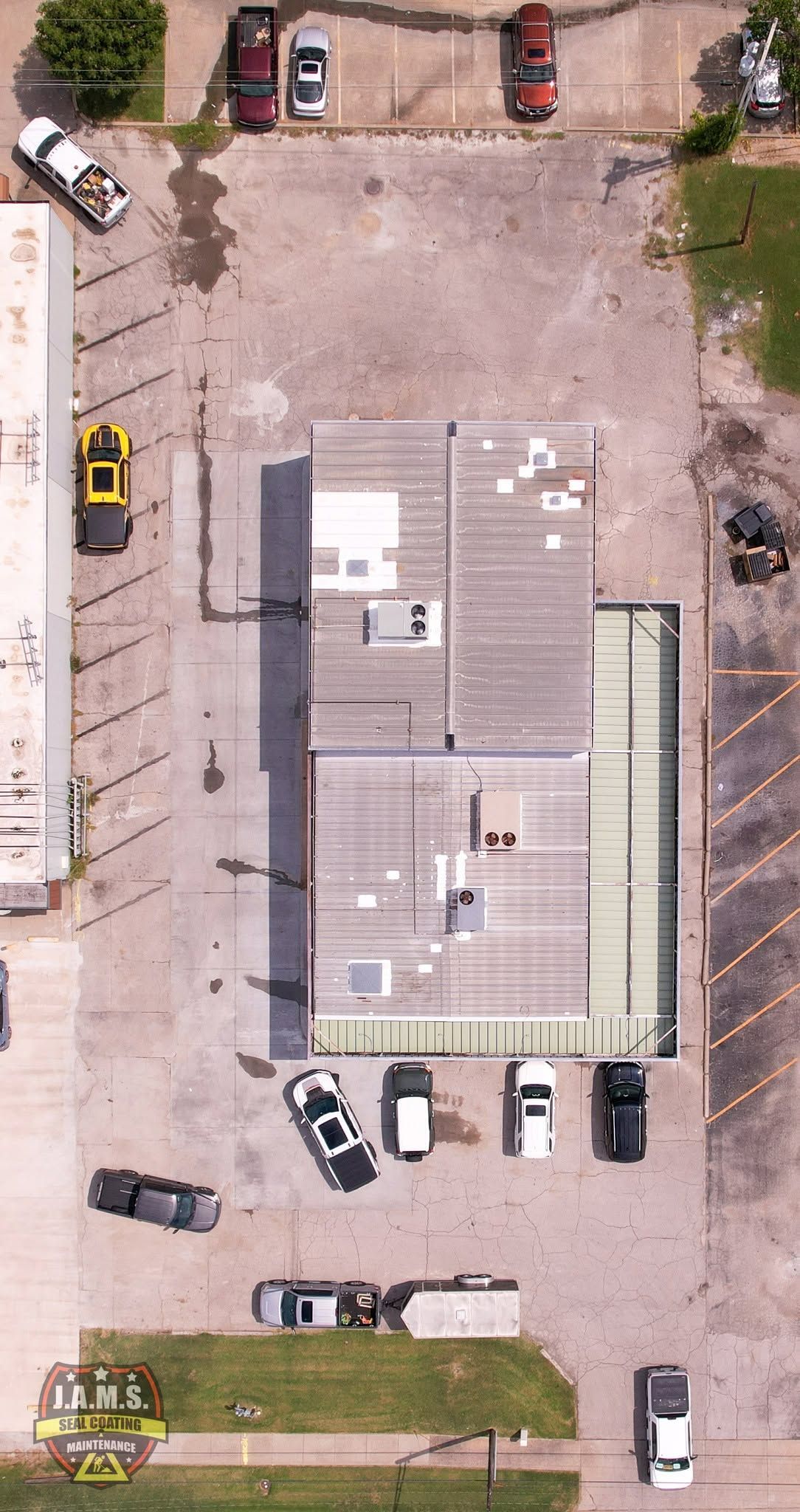 Aerial view of a large gray-roofed building with parked cars and trucks in a lot