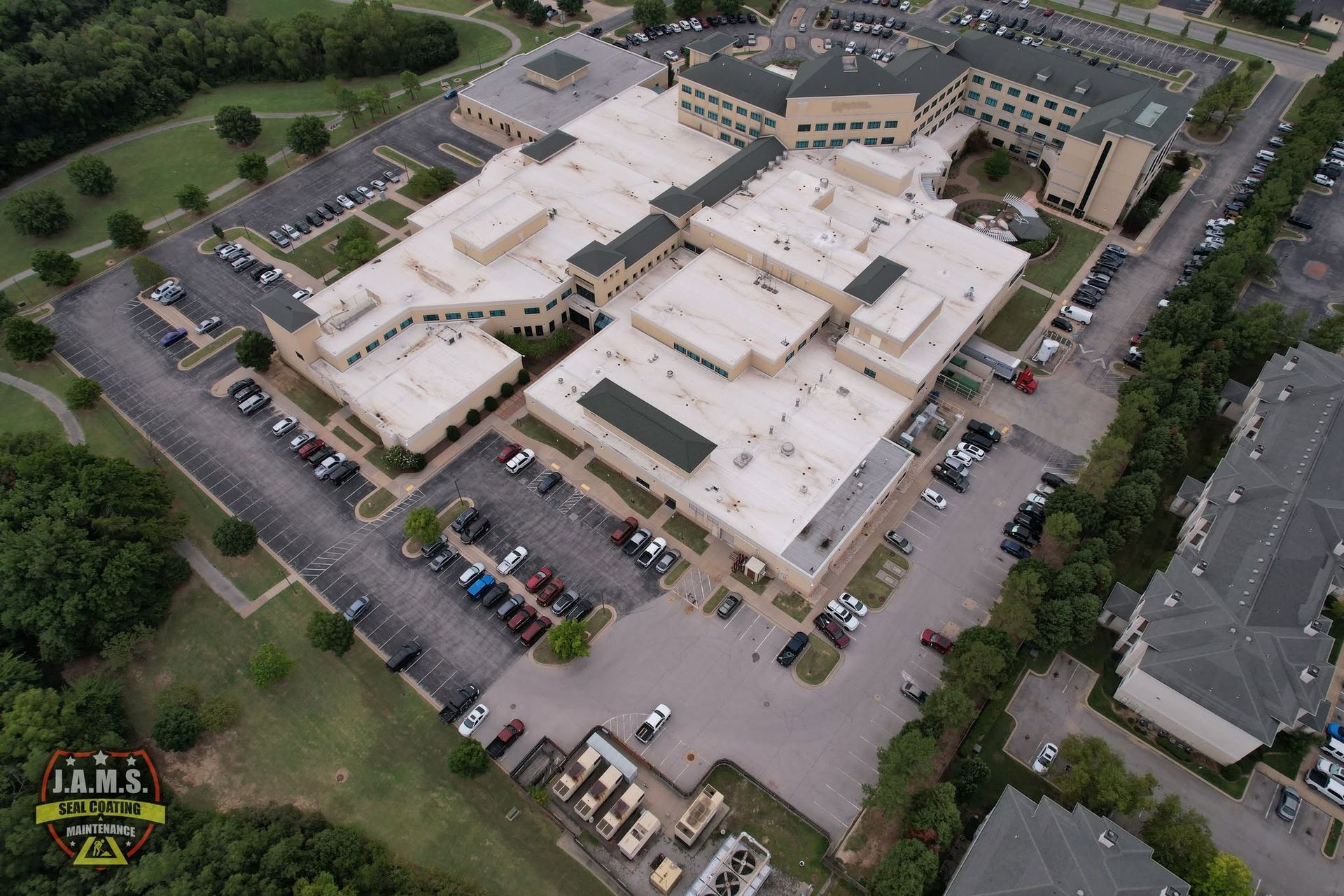 Aerial view of a large beige building complex with parking lots and surrounding trees.