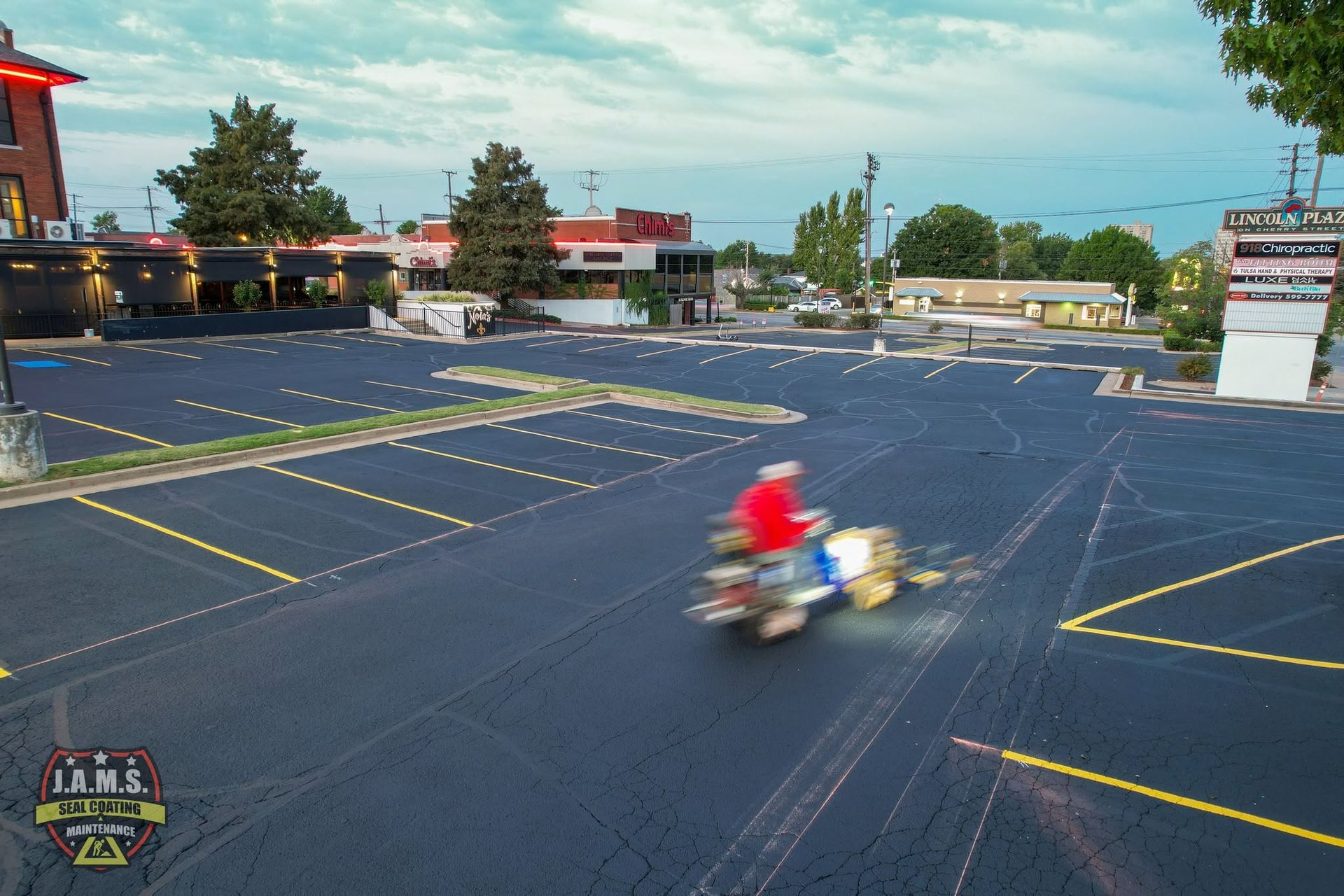 Motorcycle rider in a red shirt speeding across an empty parking lot on a sunny day