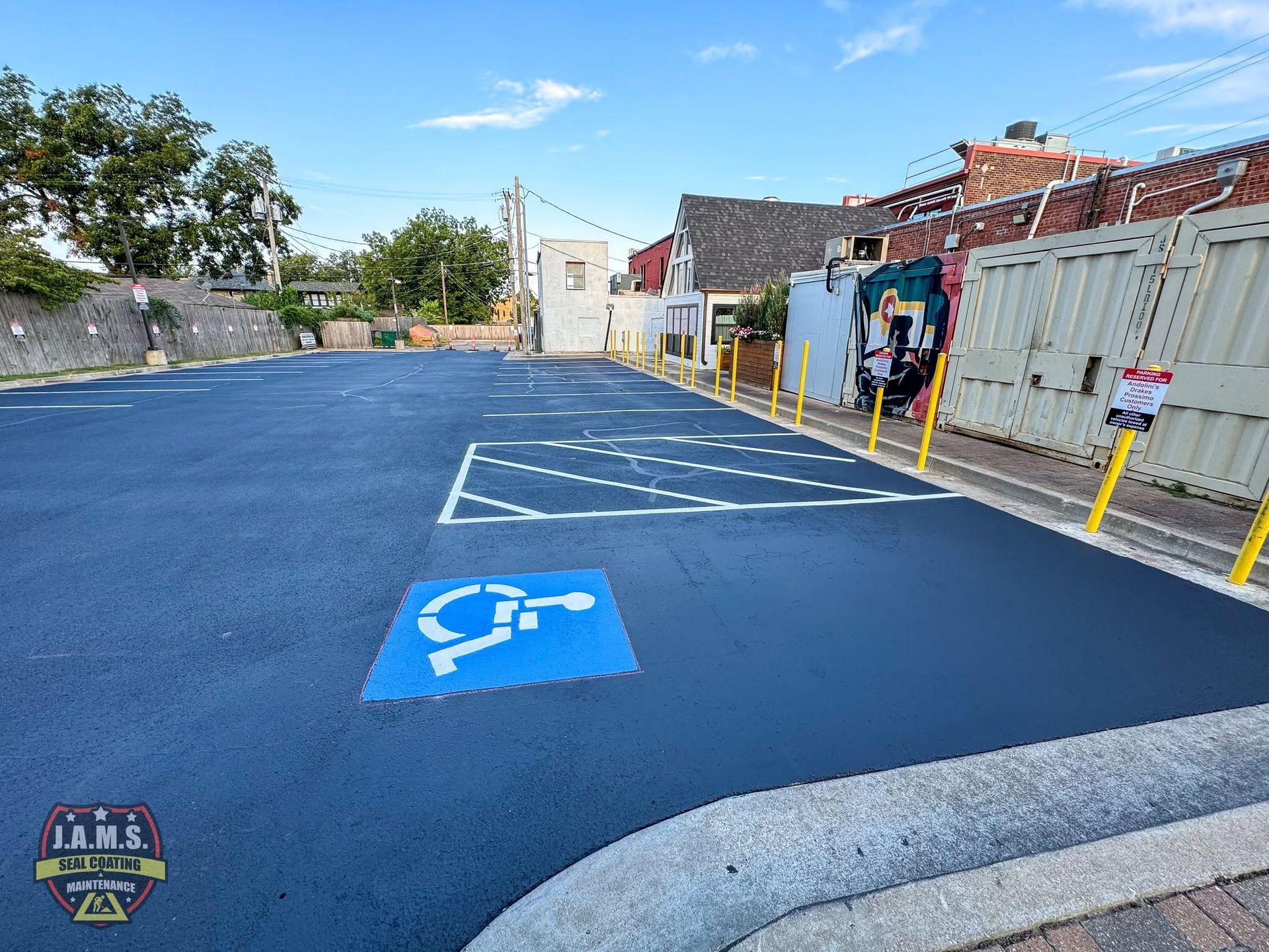 Blue accessible parking spaces in a mostly empty lot beside a low building and fence