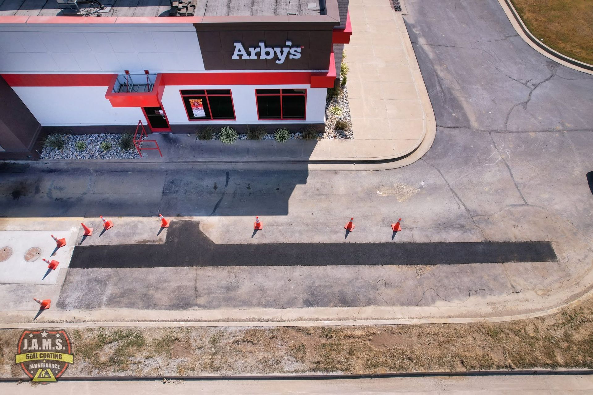Aerial view of an Arby’s storefront beside a parking lot with orange traffic cones and road markings.