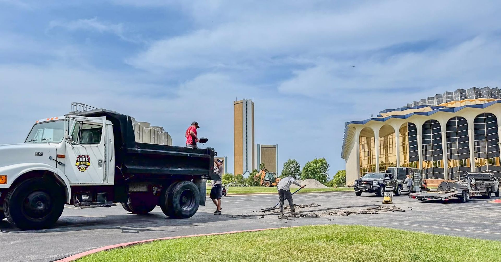 Dump truck and workers outside a yellow building under a cloudy sky.