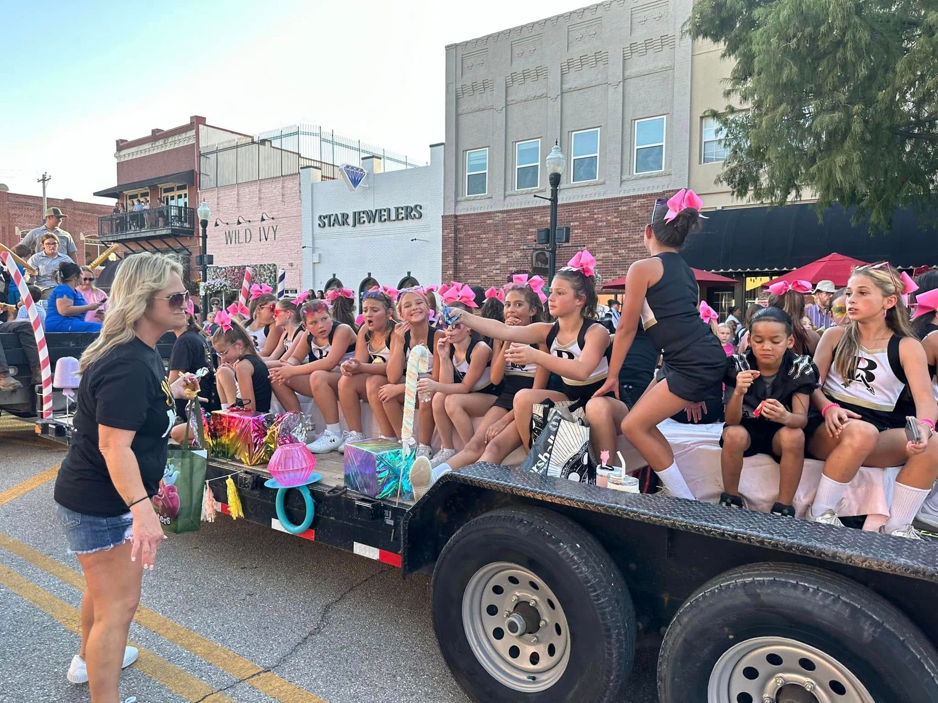 Decorated parade float with seated cheerleaders and a standing woman on a city street