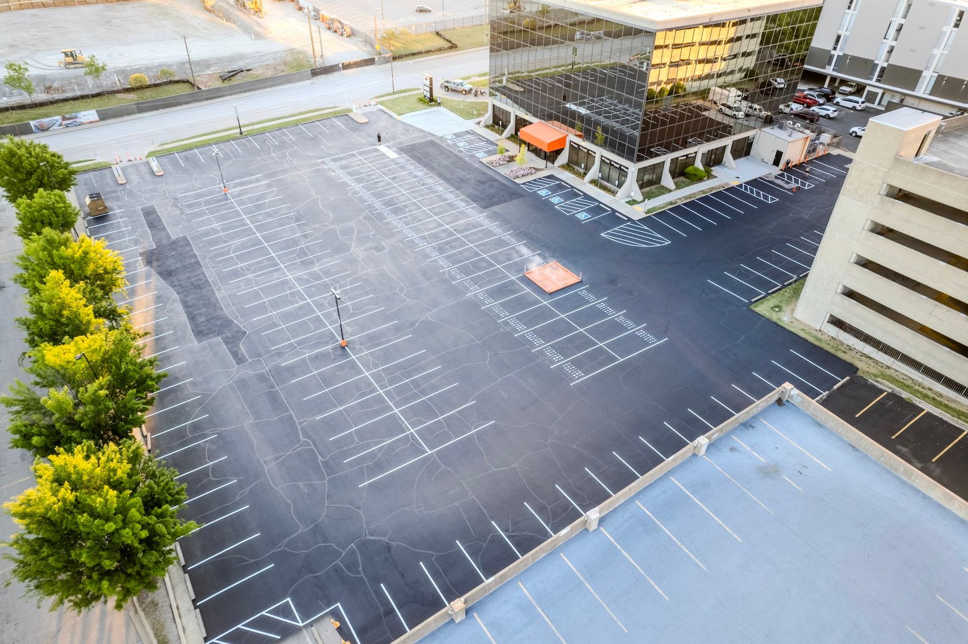 Empty parking lot beside office buildings, with marked spaces and a few trees.