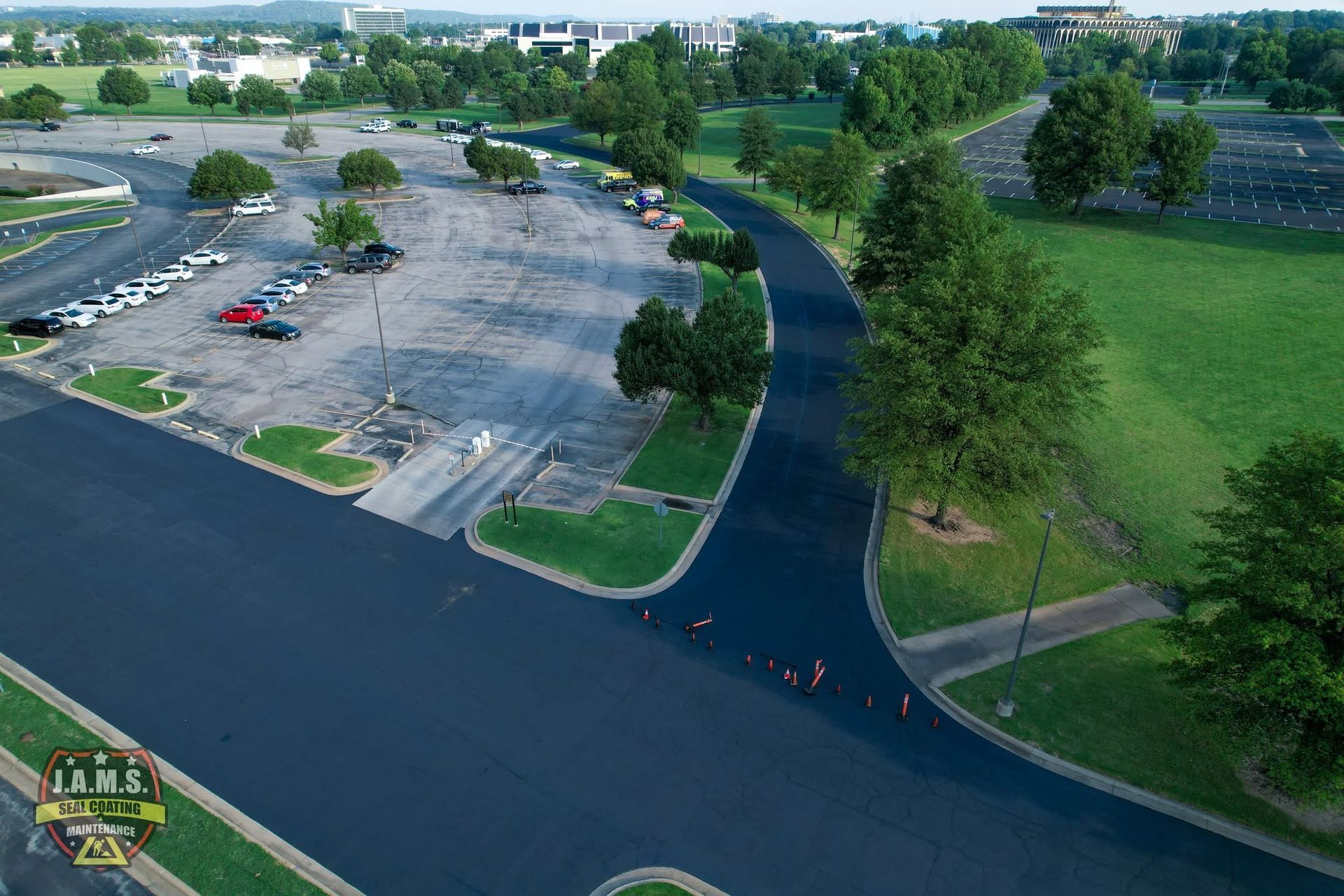 Aerial view of a parking lot beside a tree-lined road and grassy field.