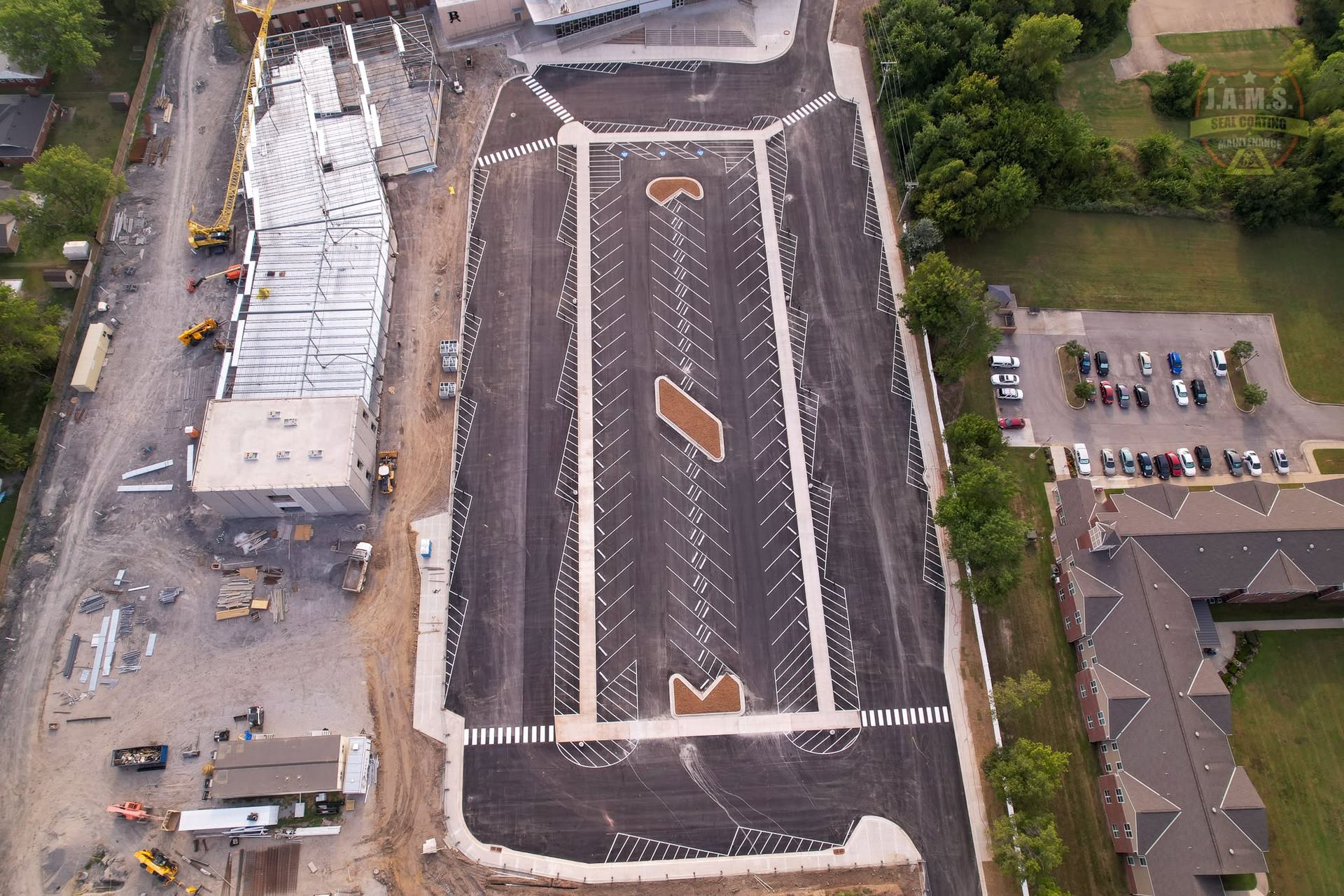 Aerial view of a large parking lot with many vehicles, a white-roofed building, and nearby houses.