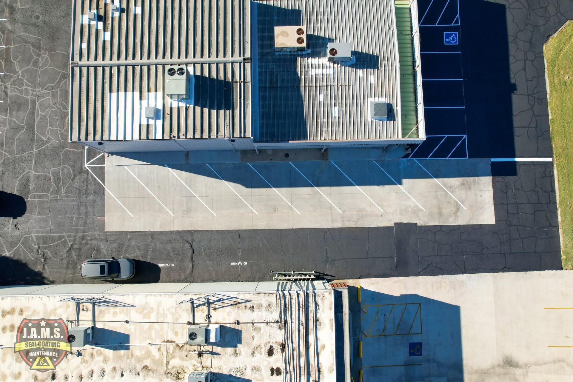 Aerial view of a rooftop and parking lot with two parked cars and long shadows.
