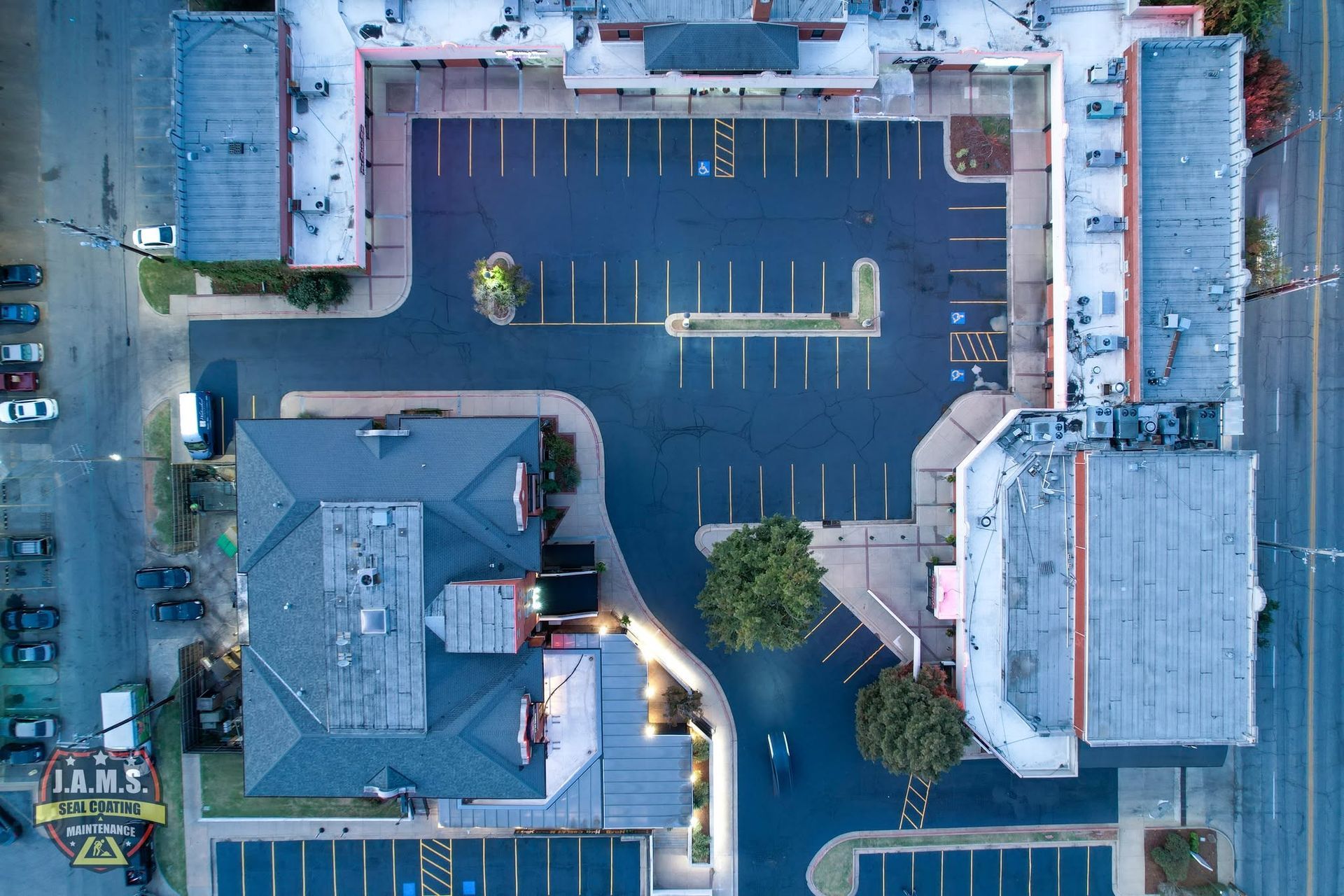 Aerial view of an empty parking lot with surrounding buildings and a few trees.