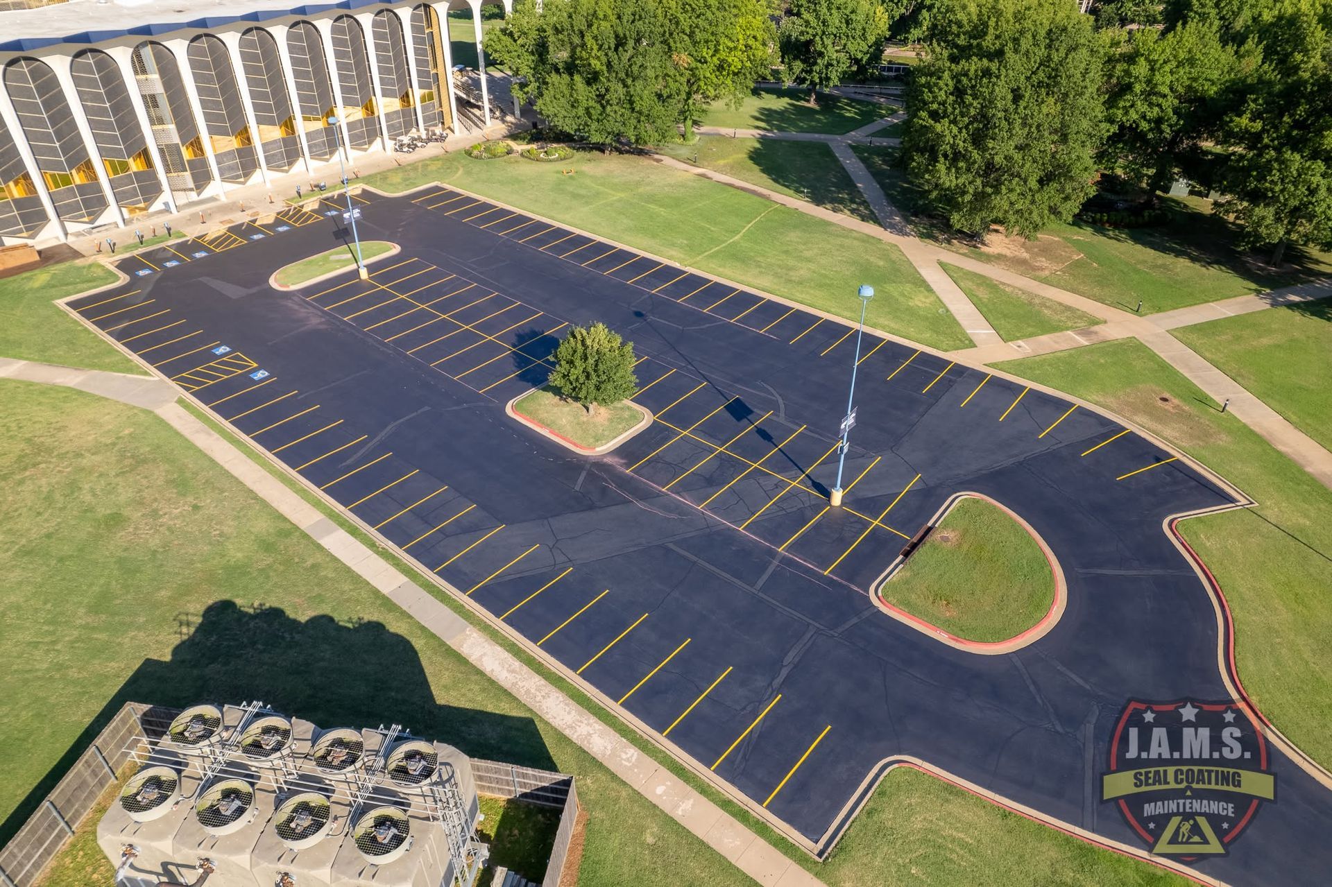 Aerial view of an empty blacktop parking lot with yellow lines beside a building and trees