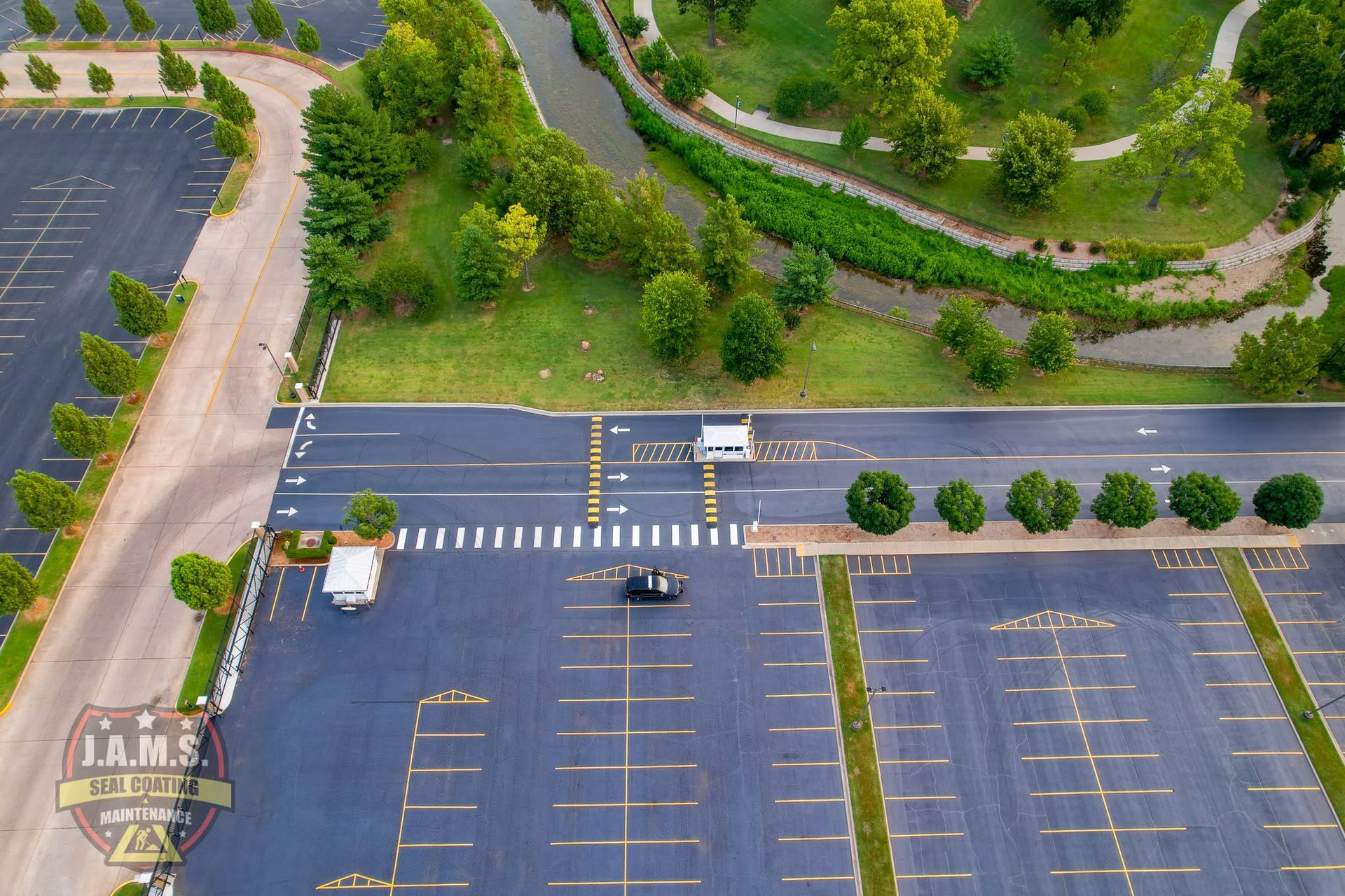 Aerial view of an empty parking lot with a few cars, lined trees, and a road beside green landscaping.