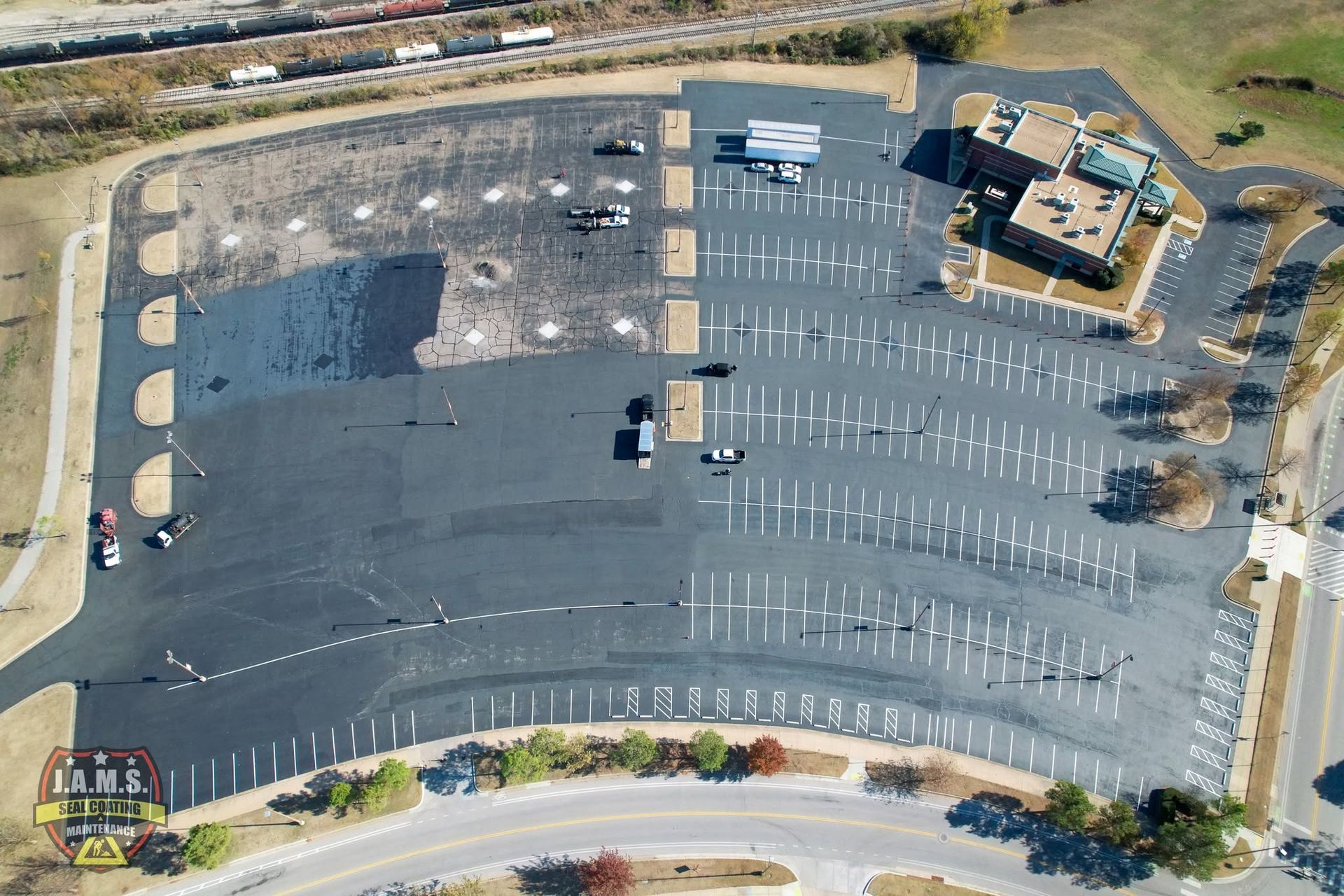 Aerial view of a mostly empty parking lot beside a building and road, with a few parked cars and painted spaces.
