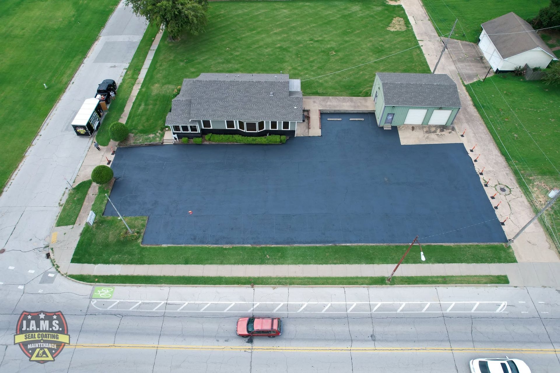 Aerial view of a small roadside building with a large blue paved lot and grassy surroundings.