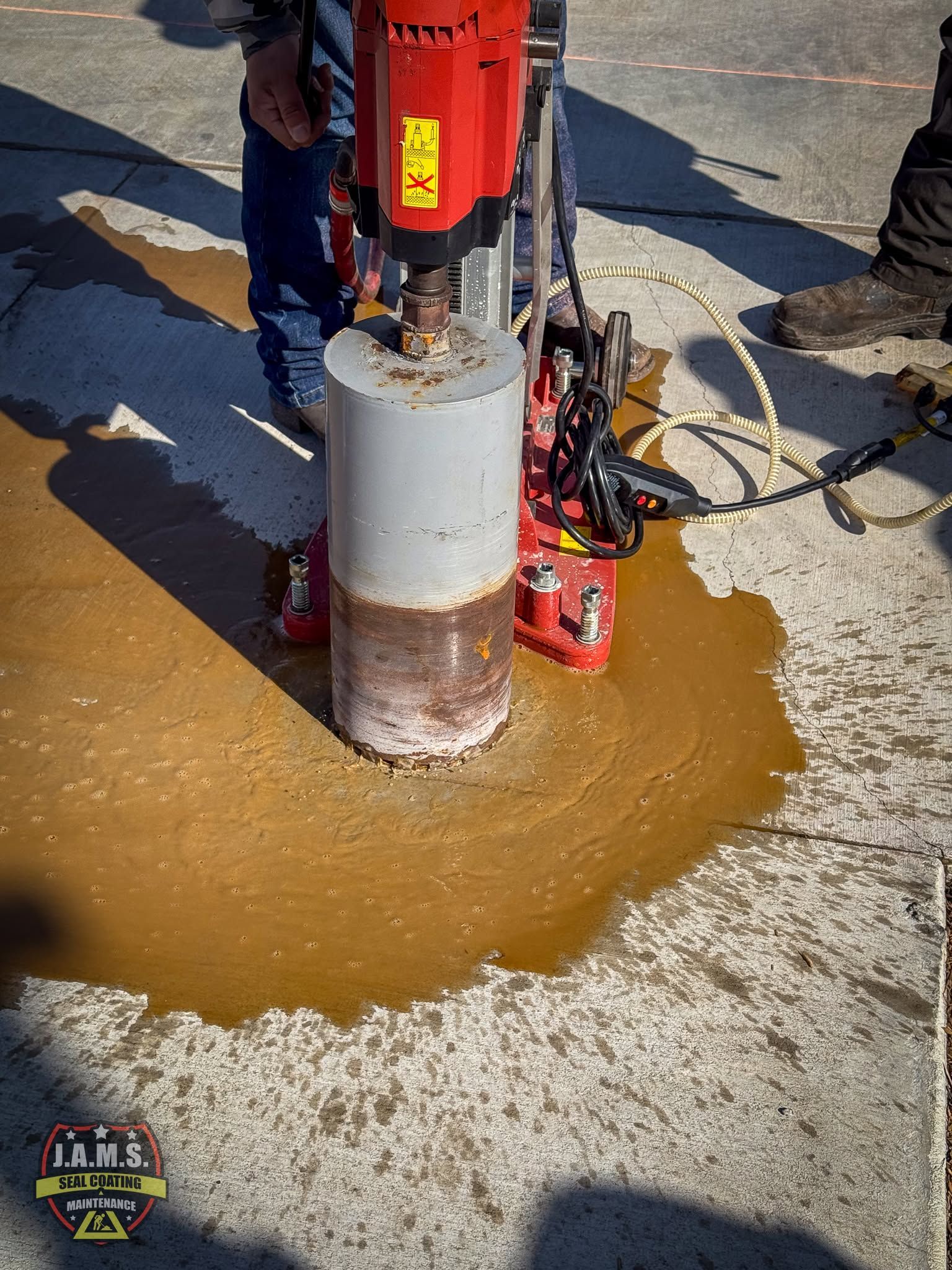 Drilling rig boring into pavement, with muddy water pooled around the drill head and core sample