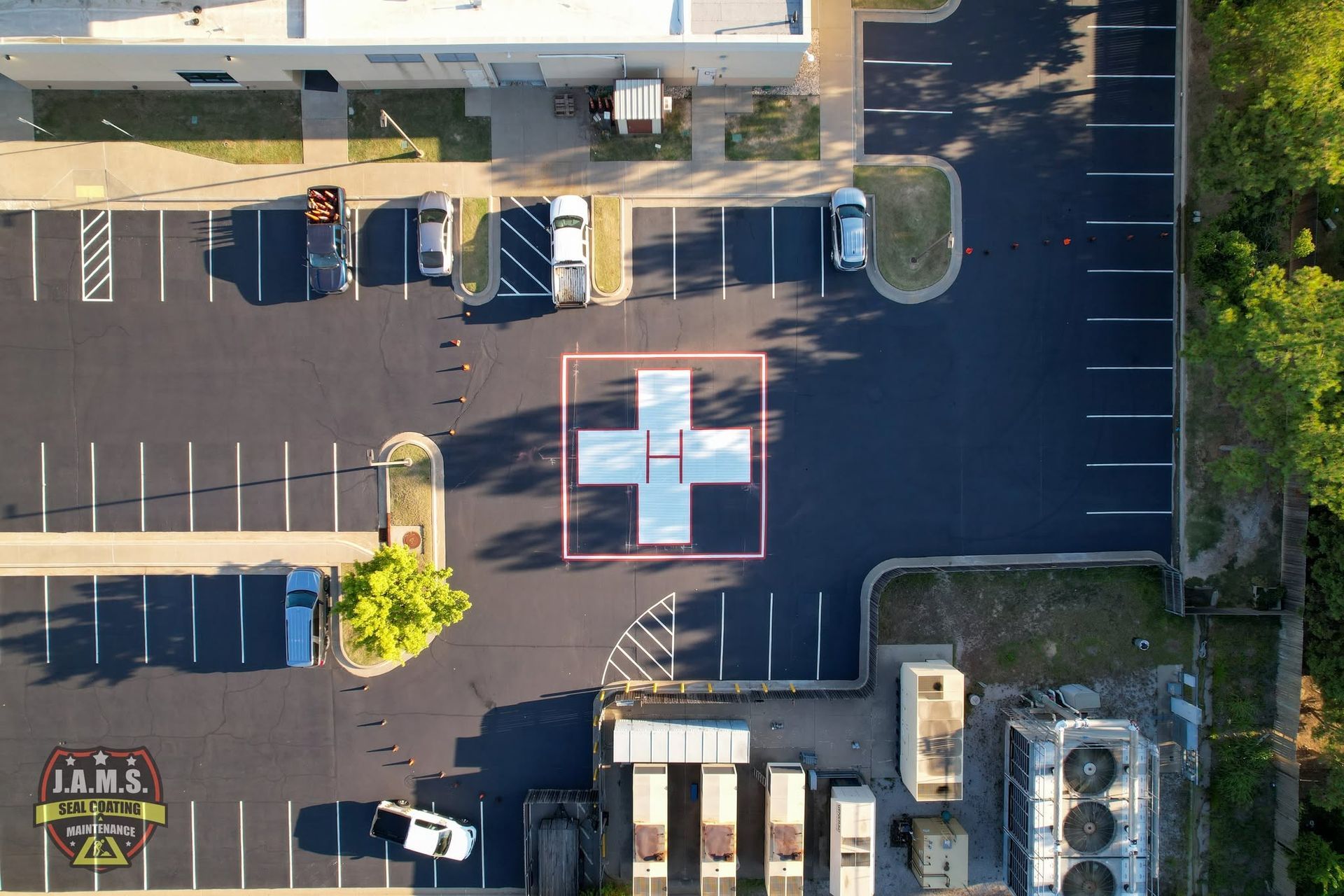 Aerial view of a parking lot with a marked medical landing pad near parked vehicles and buildings.