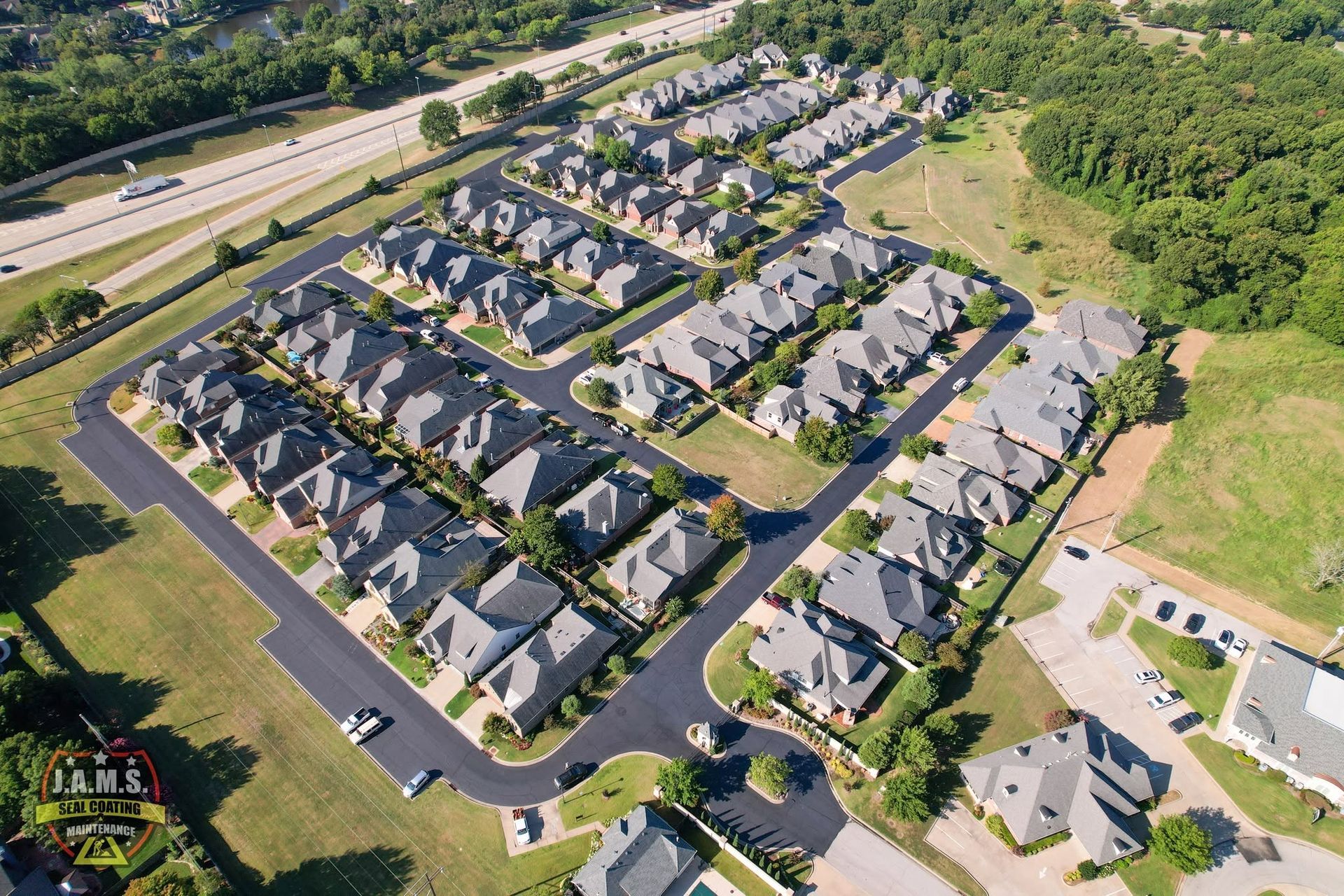 Aerial view of a suburban townhouse neighborhood with roads, parking, and trees nearby.