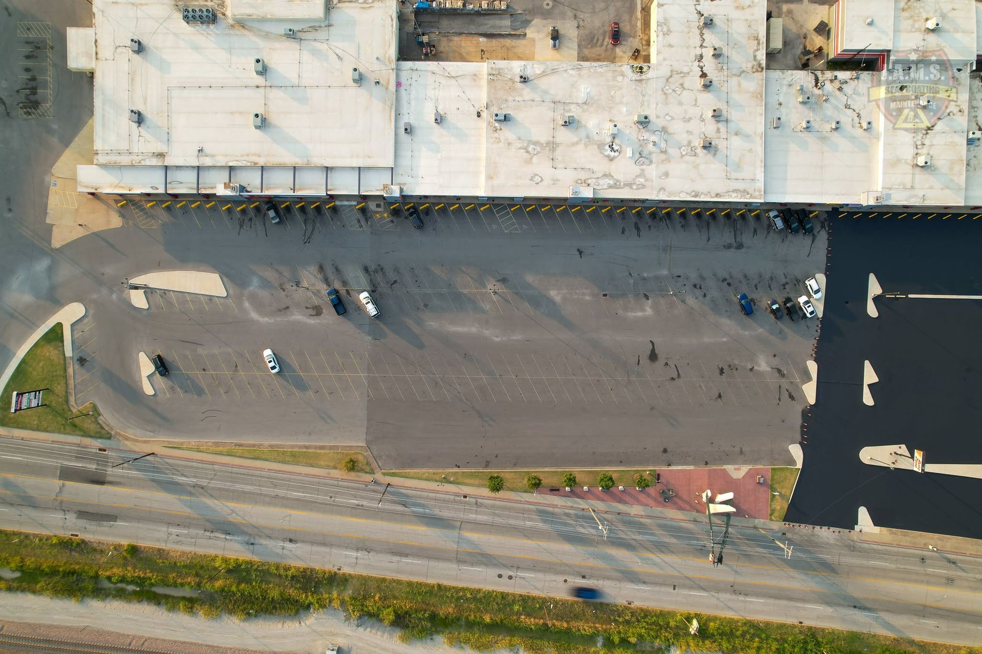 Aerial view of a parking lot beside a building, with a few cars and a road at the bottom.