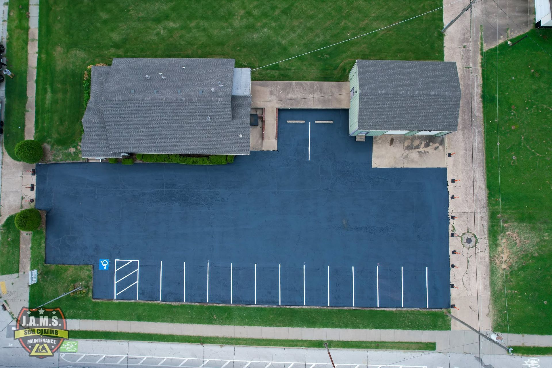 Aerial view of a building with a large blue parking lot and white-lined spaces beside grassy areas.