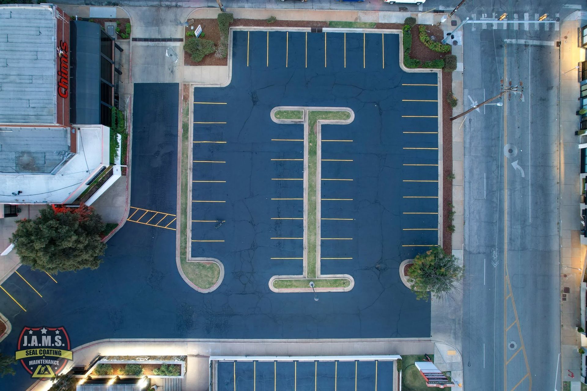 Aerial view of an empty parking lot with painted lanes and surrounding buildings and streets.