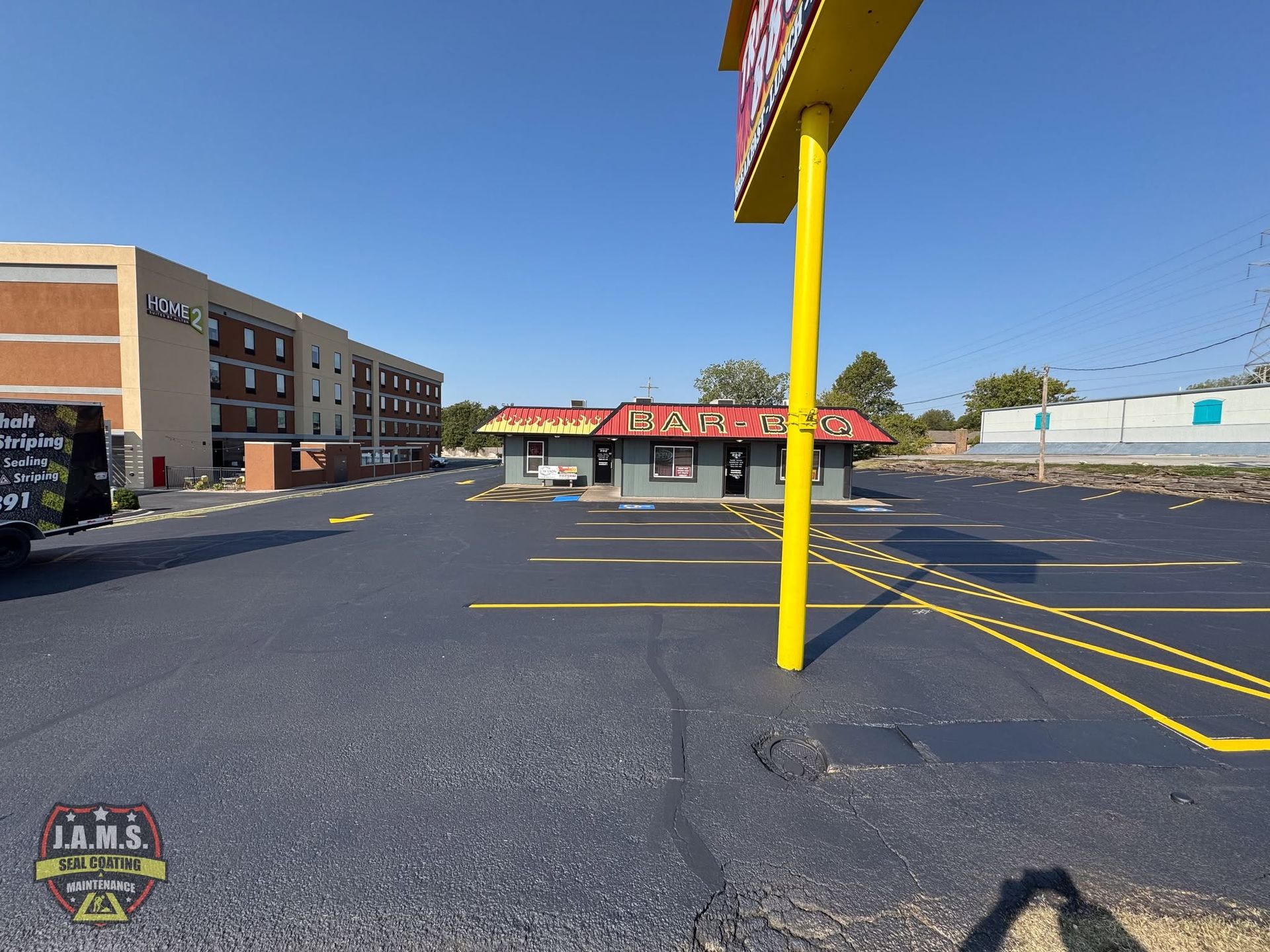 Empty parking lot beside a motel and storefronts on a sunny day, with a yellow signpost in the foreground