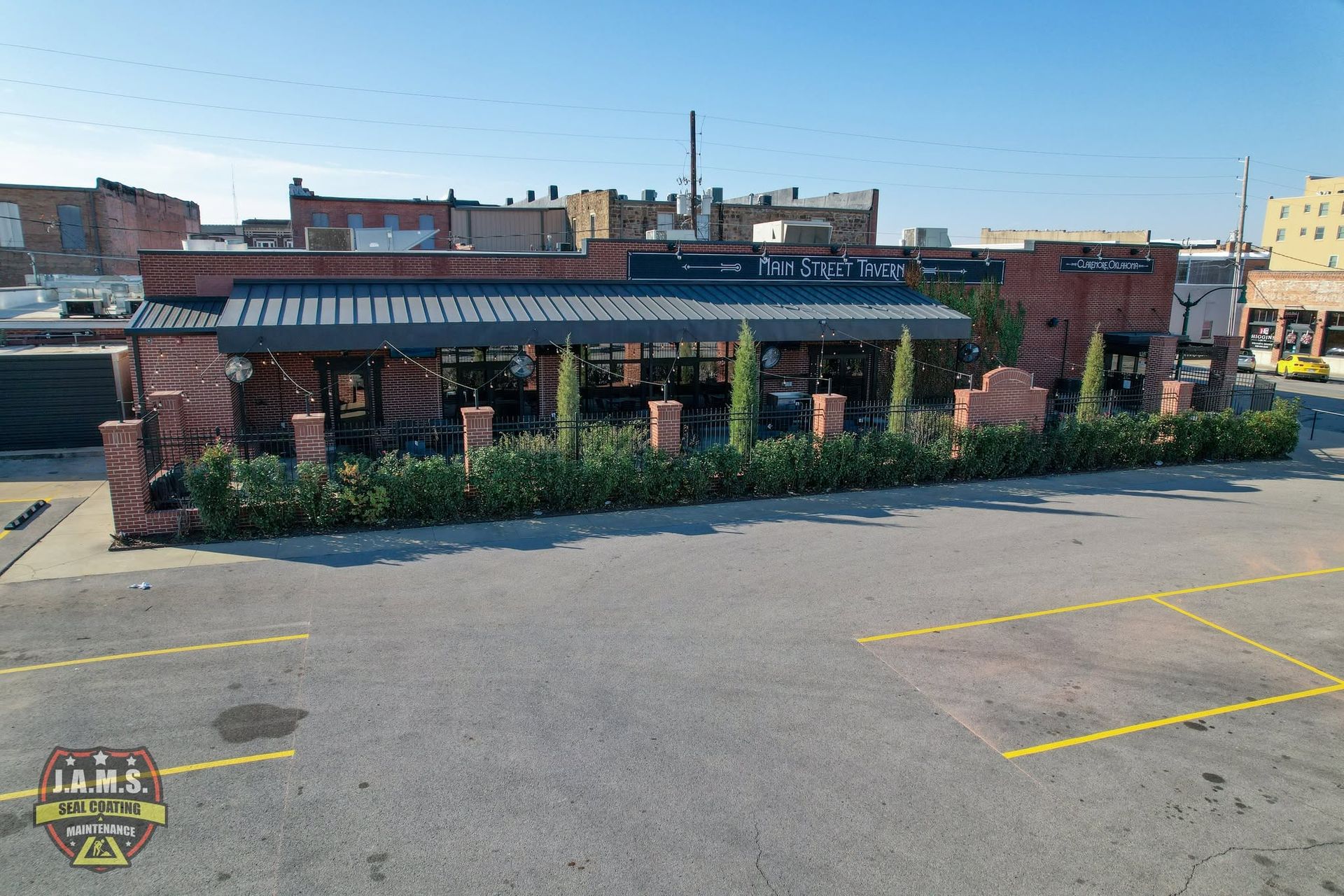 Brick restaurant with striped awning and outdoor plants beside an empty parking lot.