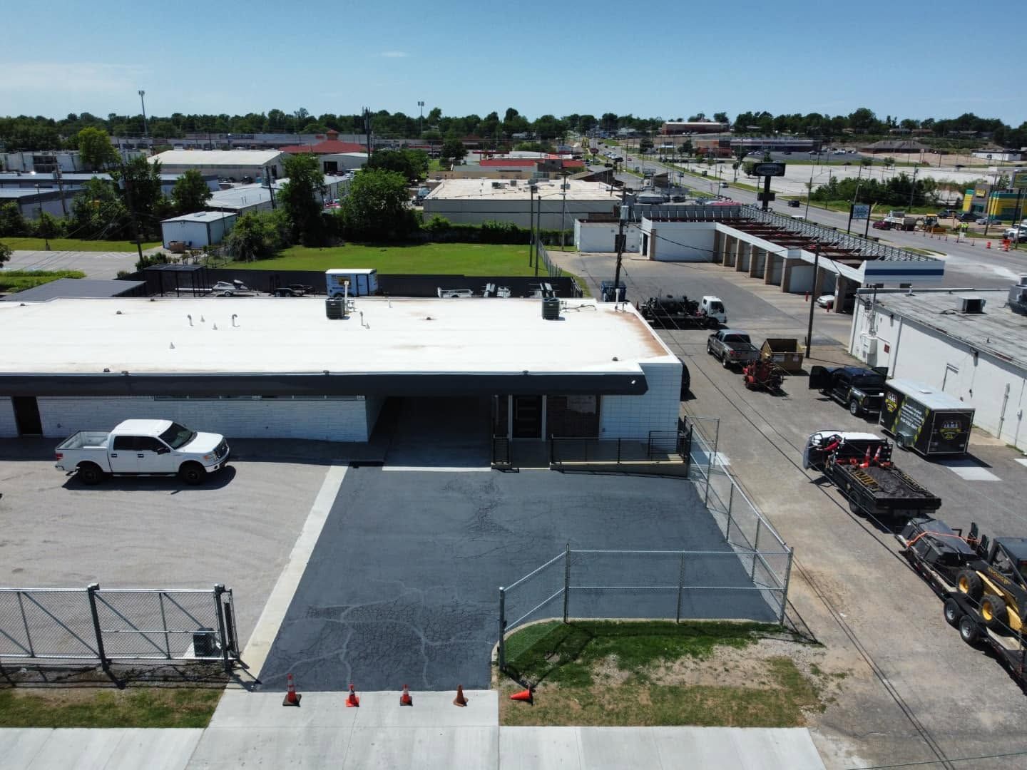 Aerial view of an industrial lot with a white-roofed building, parked truck, fenced area, and nearby streets