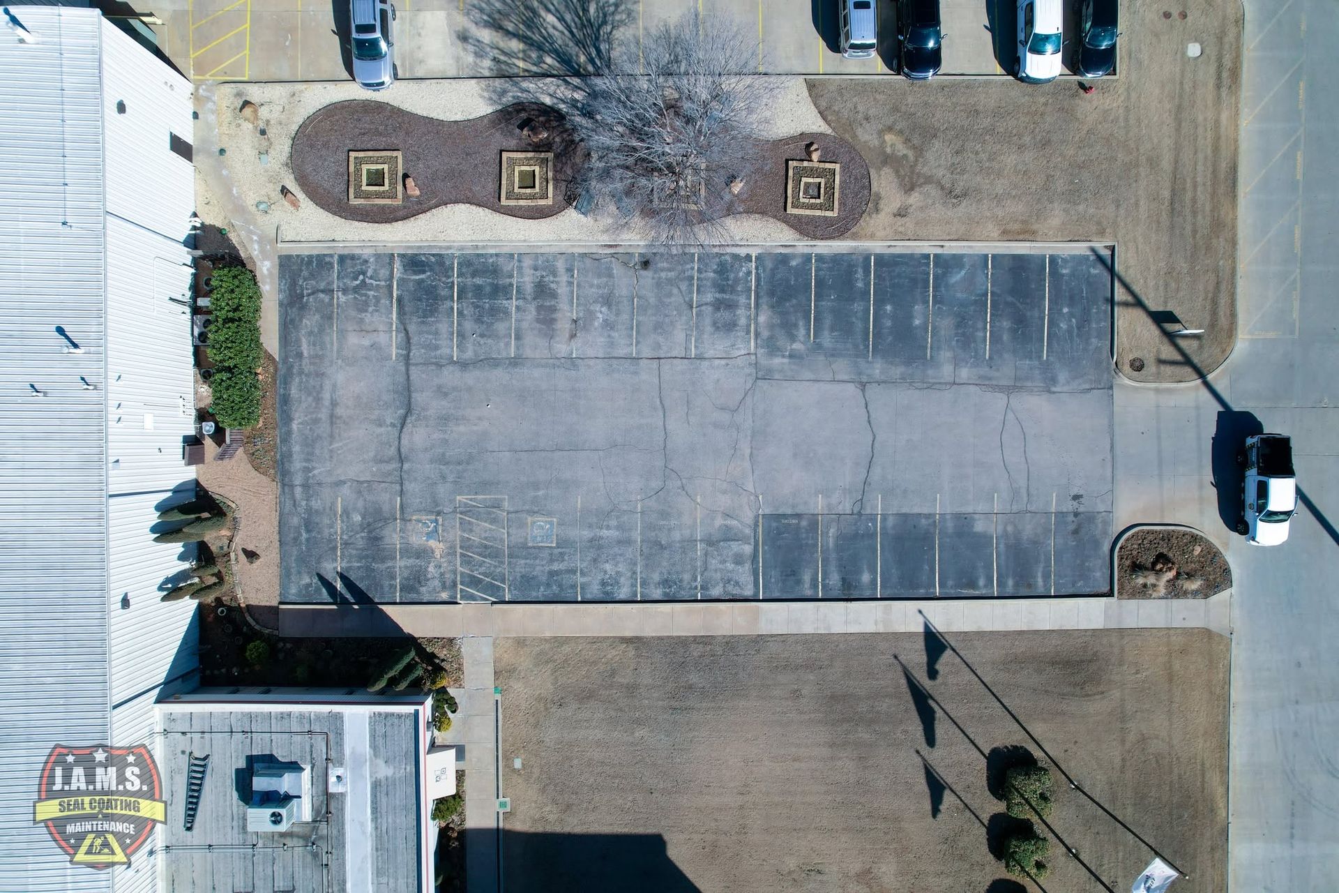 Aerial view of a large empty concrete parking lot with a few cars and surrounding buildings.
