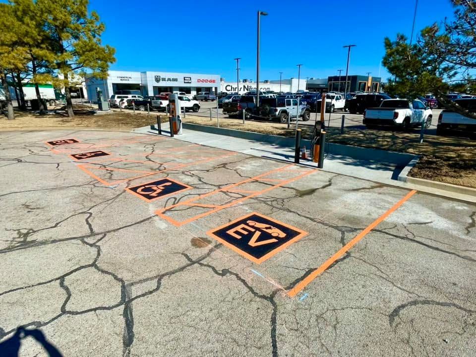 Accessible parking spaces with orange markings in a sunny parking lot by a sidewalk and road.