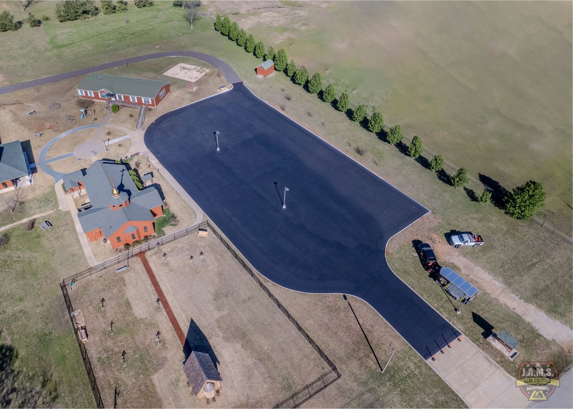 Aerial view of a paved driving course beside a building, with trees and open fields nearby.