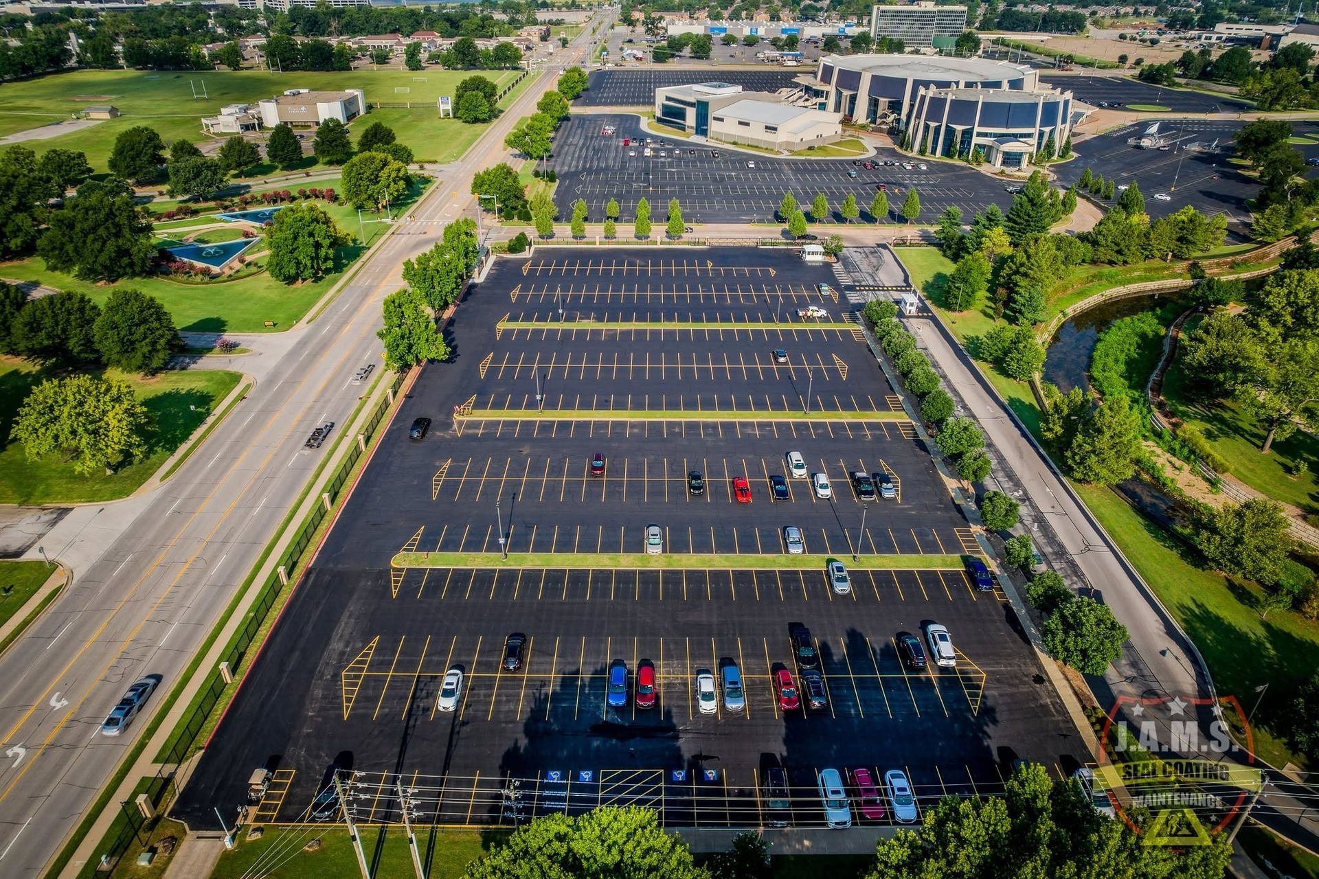 Aerial view of a nearly empty parking lot beside a large building and green landscape