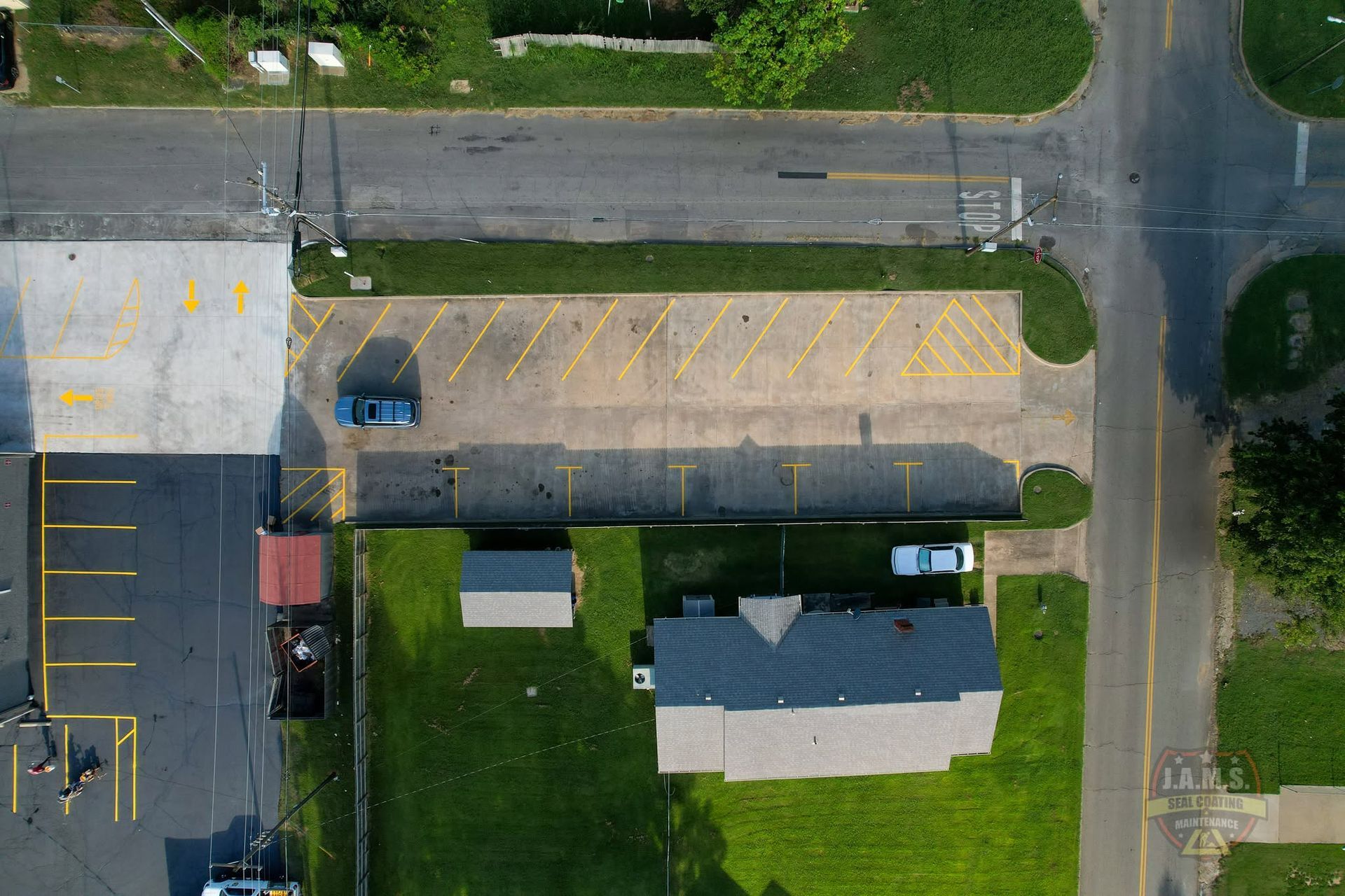 Aerial view of a parking lot, road, and small building with a blue vehicle nearby.