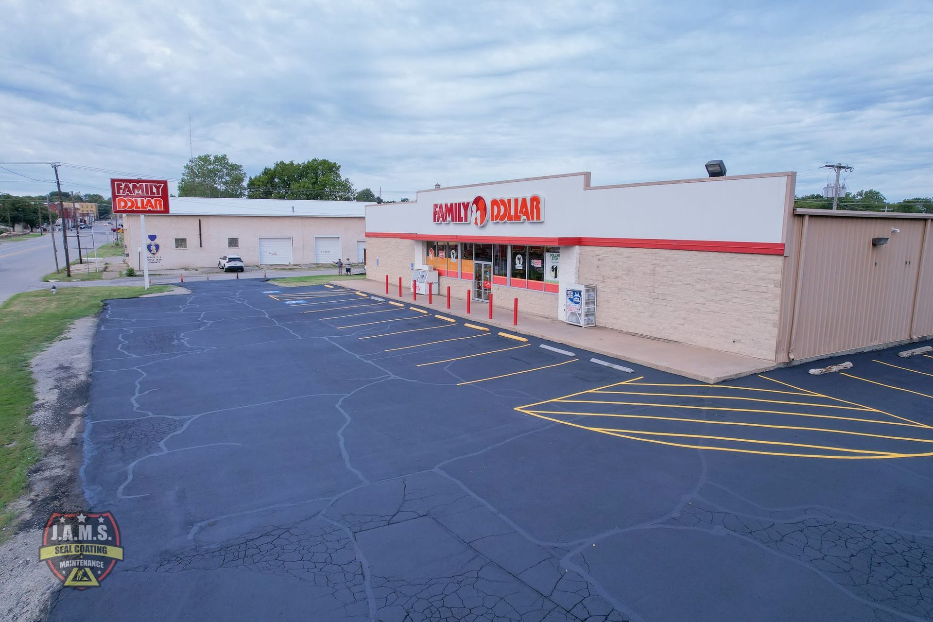 Strip mall storefront with a red sign, empty parking lot, and overcast sky