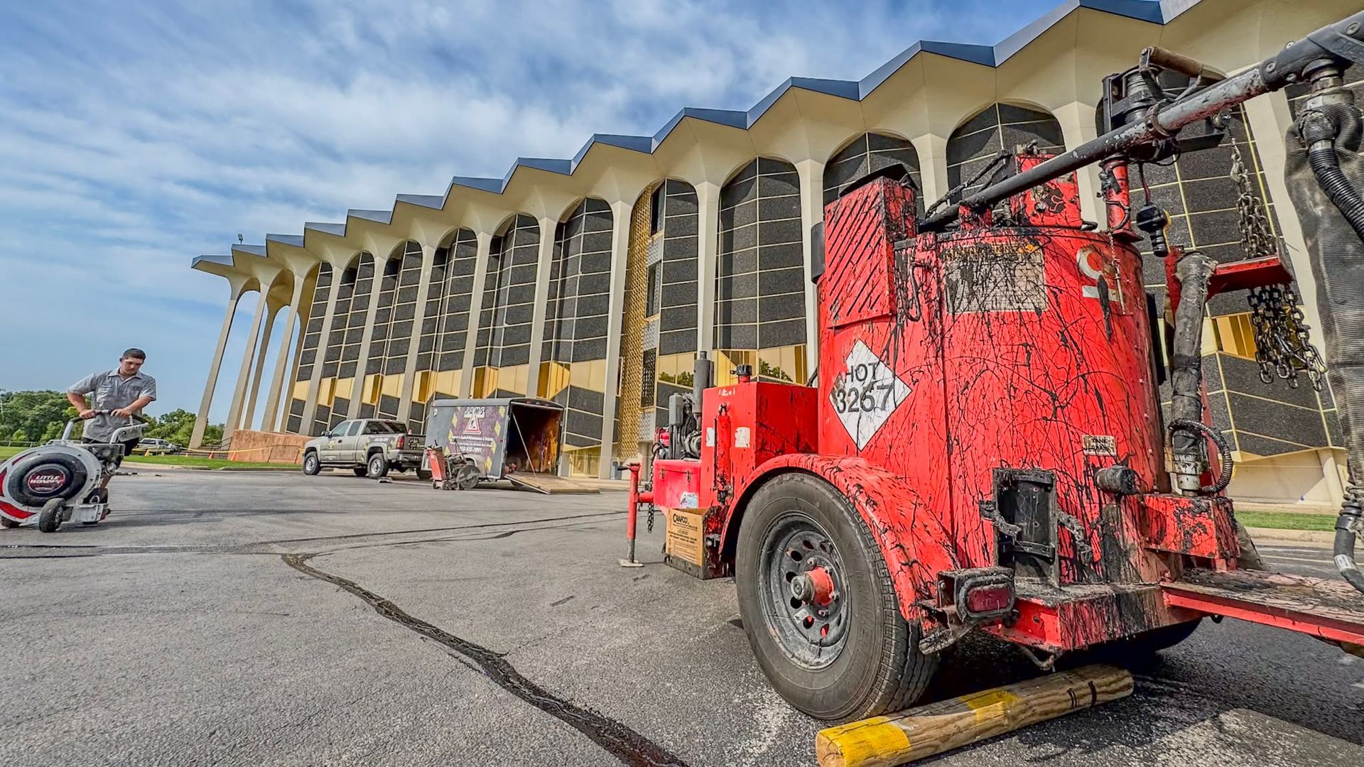 Red utility truck parked outside a large building with columns; a motorcycle is at left under a cloudy sky.