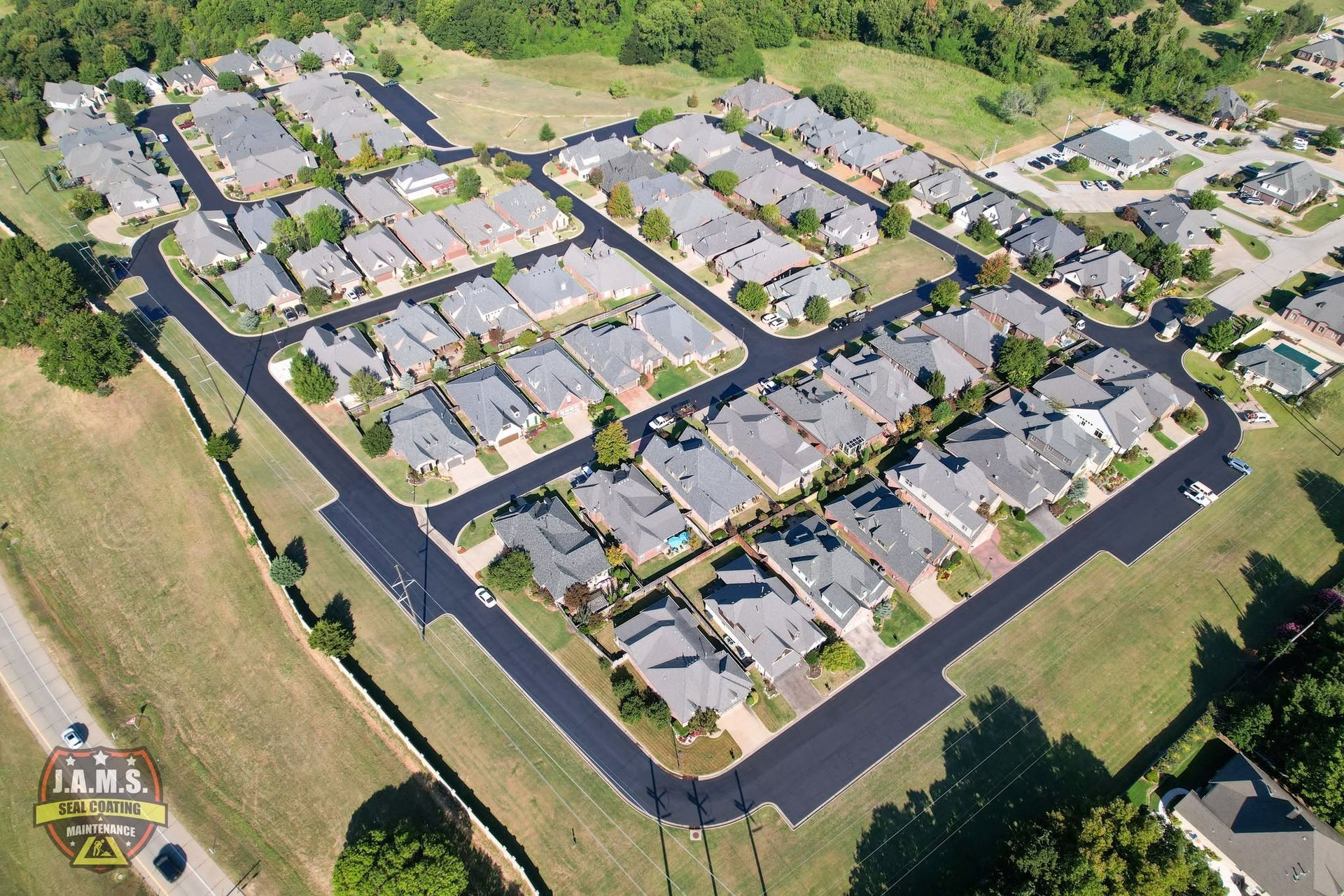 Aerial view of a suburban apartment complex with gray roofs, black roads, and surrounding green lawns.