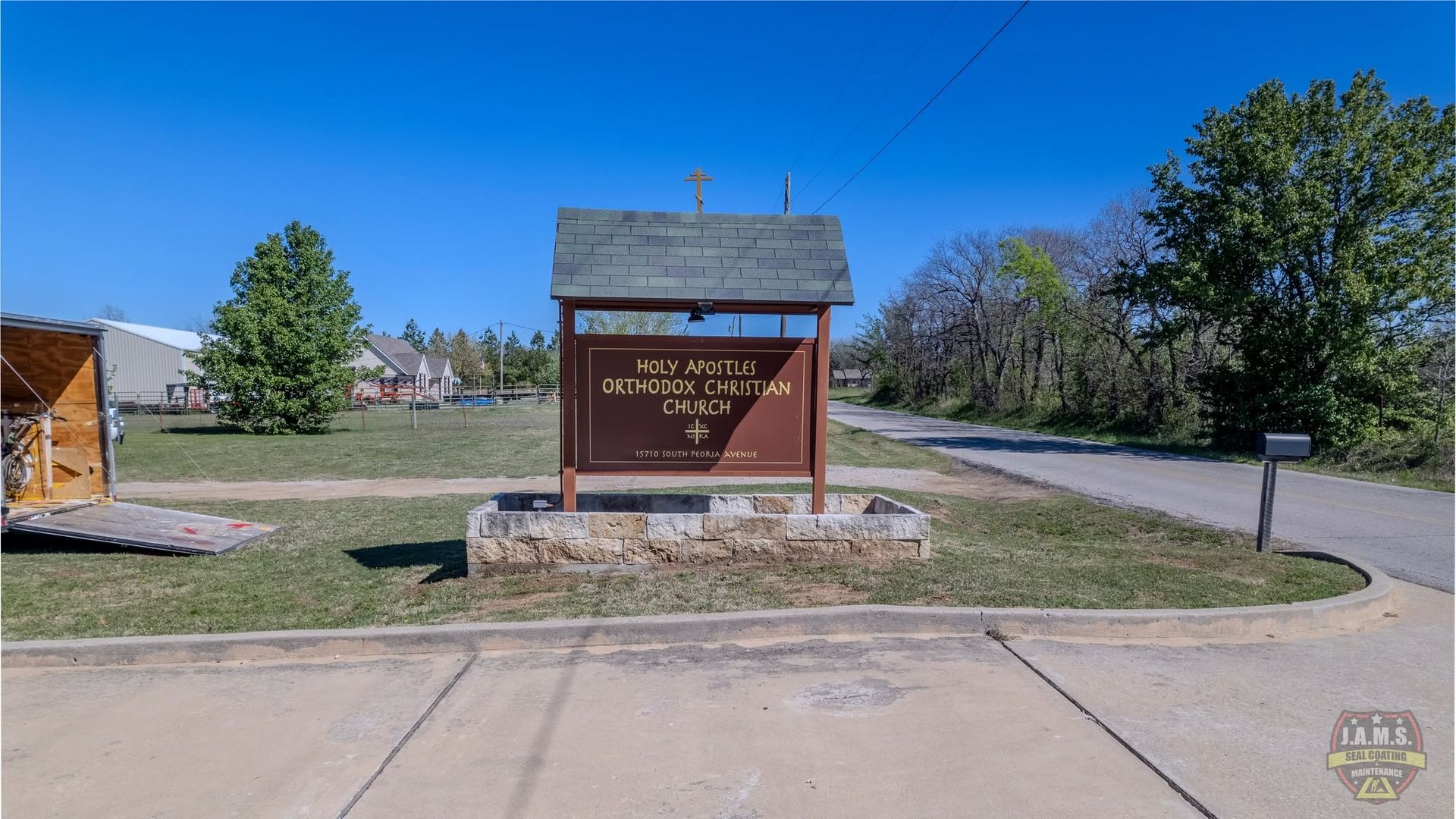 Park entrance sign on a roadside lawn under a blue sky with trees and a paved drive.