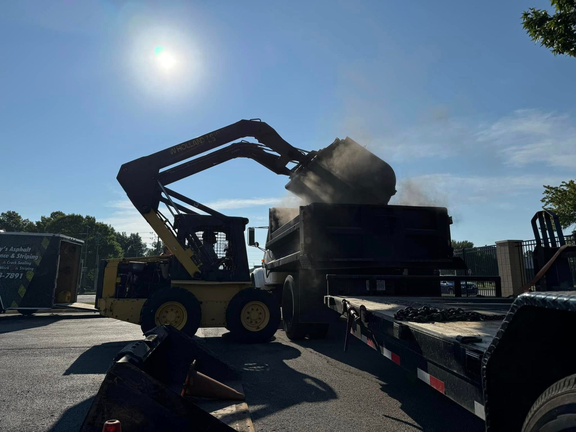 Loader dumping gravel into a truck under bright sun at a construction site