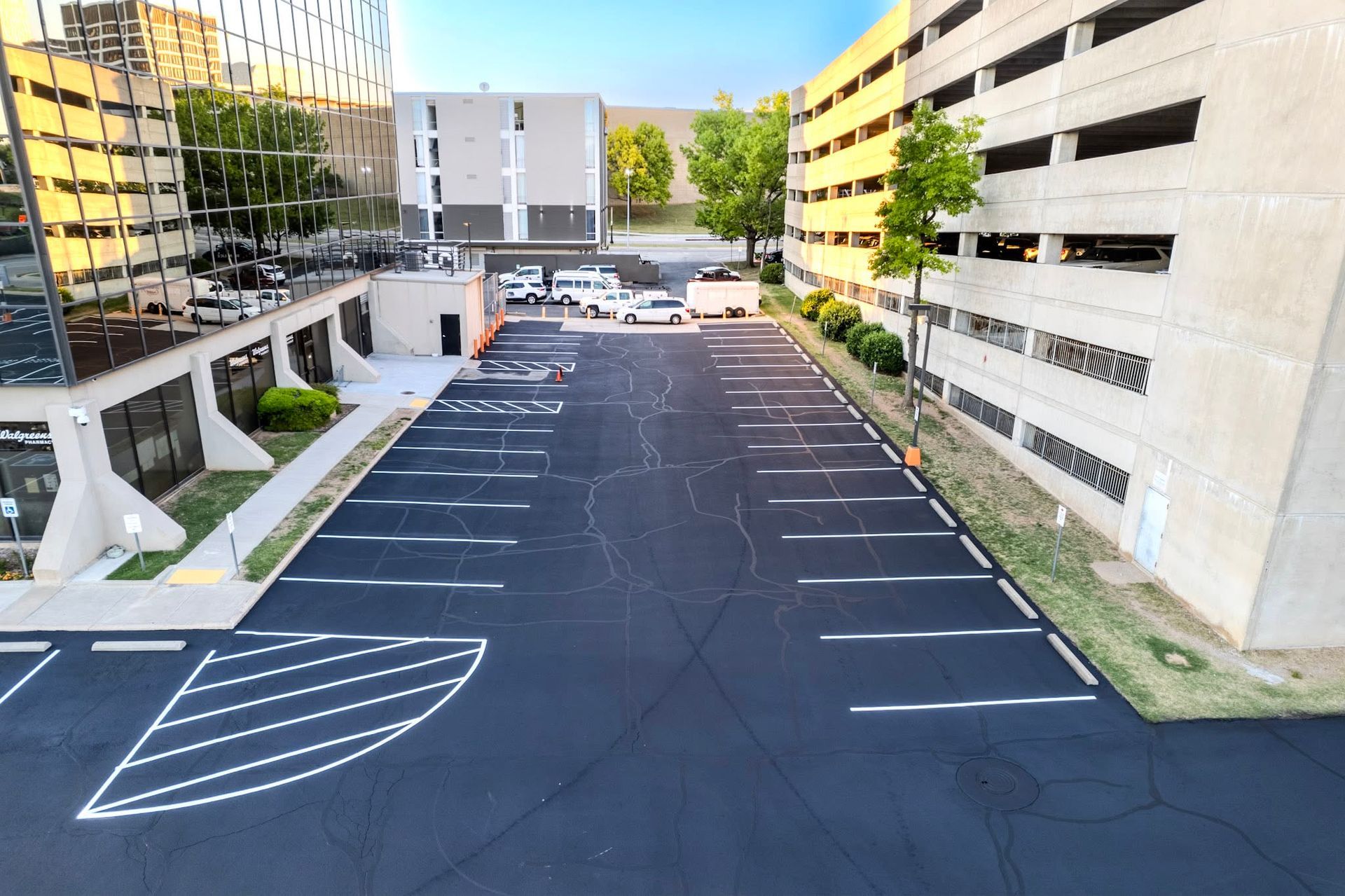 Empty parking lot beside office buildings, with painted spaces and white arrow markings